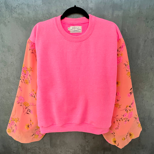 Front view of neon hot pink sweatshirt on hanger in front of cement gray background. Sweatshirt has puff sleeves with bright coral pink and marigold colorful floral.