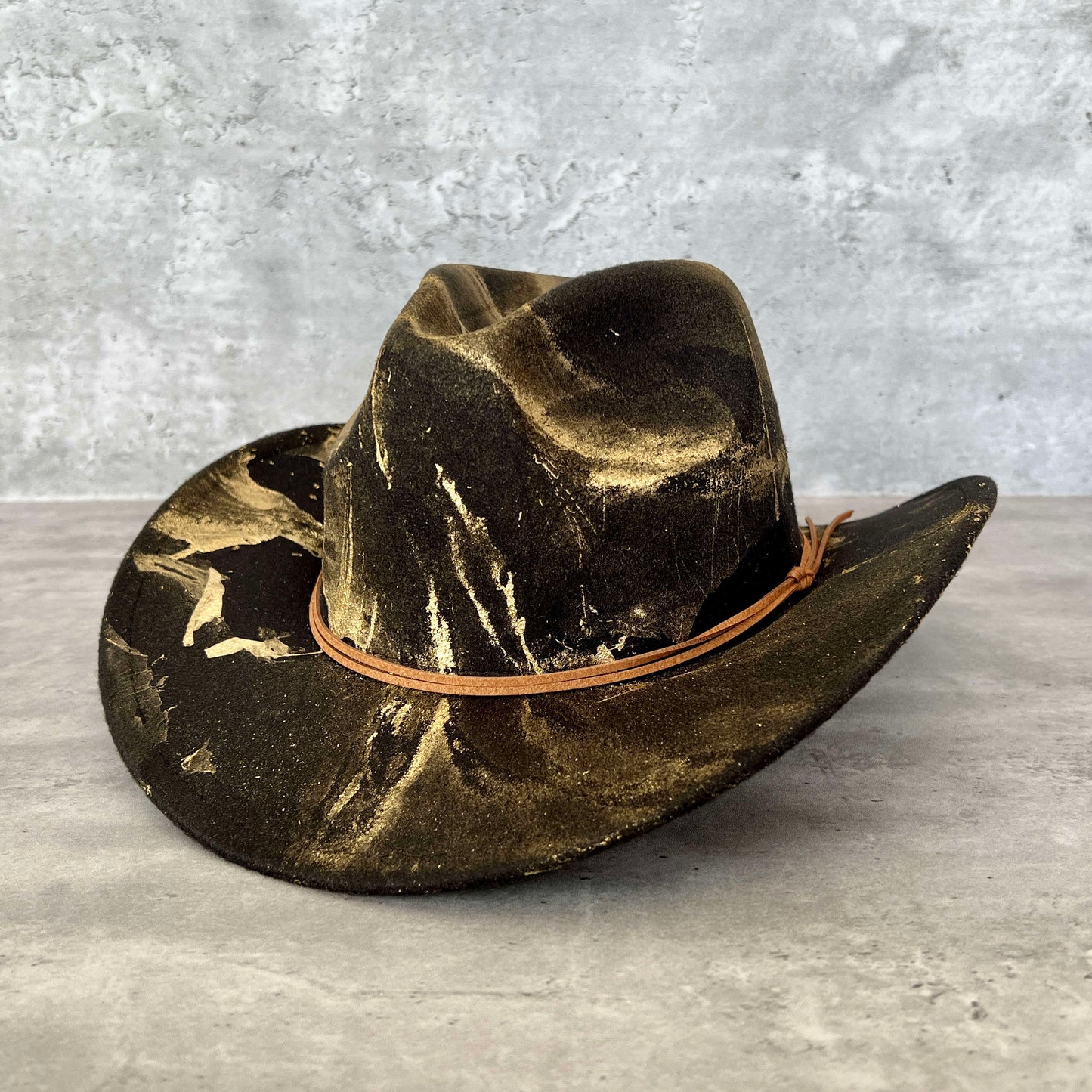 Black western cowboy hat painted with gold marbling. Has light brown faux suede cord hat band. 