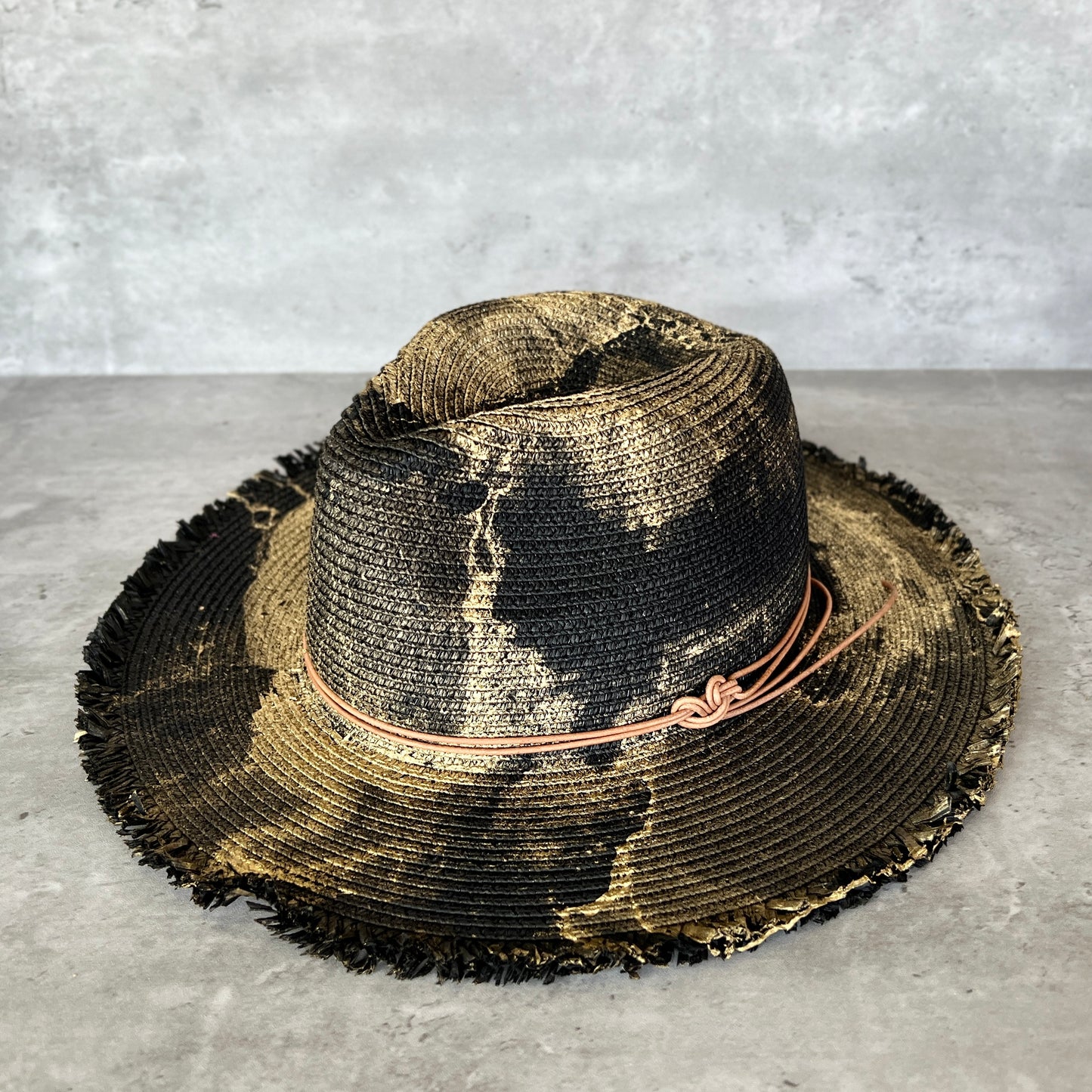 front view of black straw brim rancher hat with fringe has gold paint marbling  and brown leather faux suede cord. sun hat.