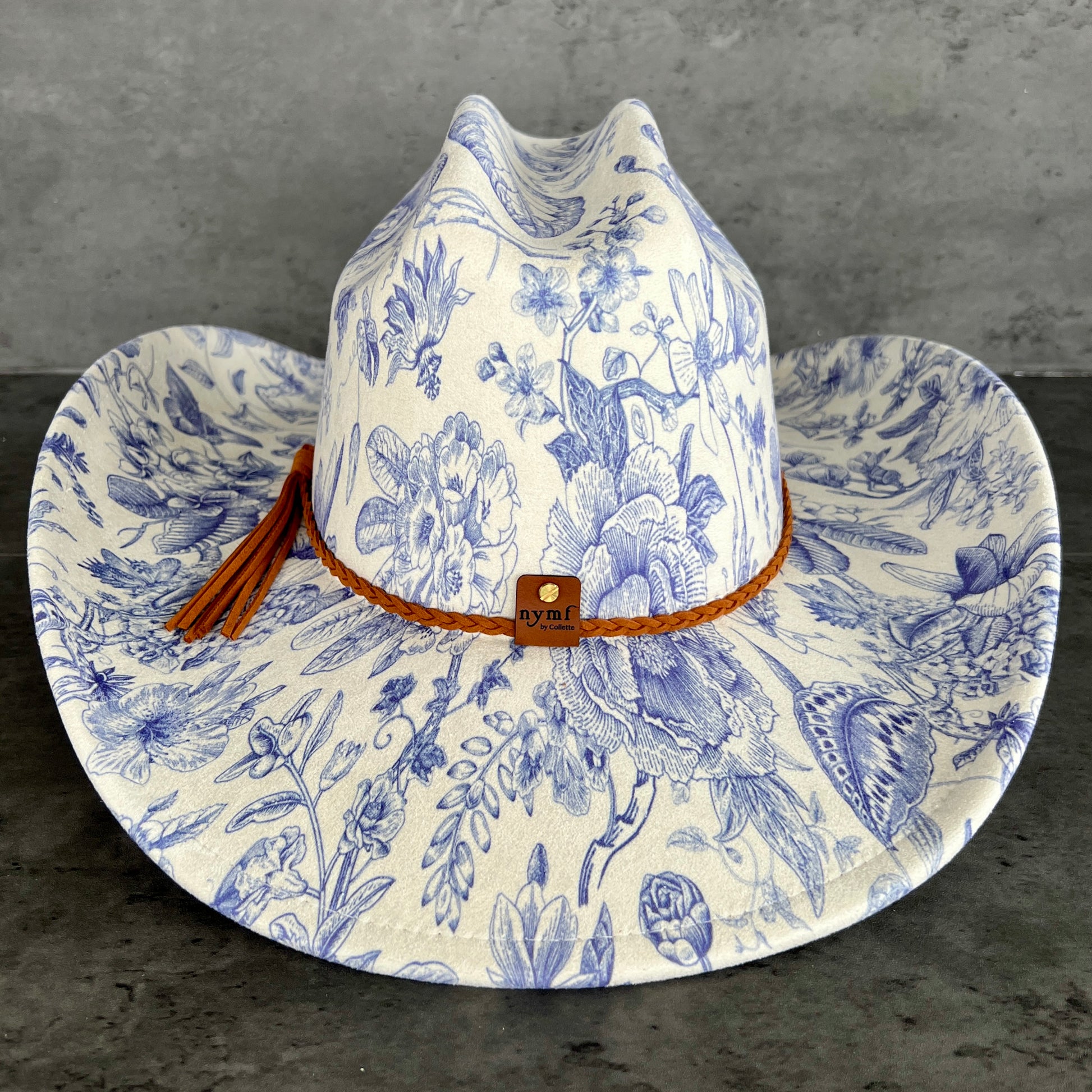 Floral-patterned cowboy hat with brown band and tassel on a dark surface.