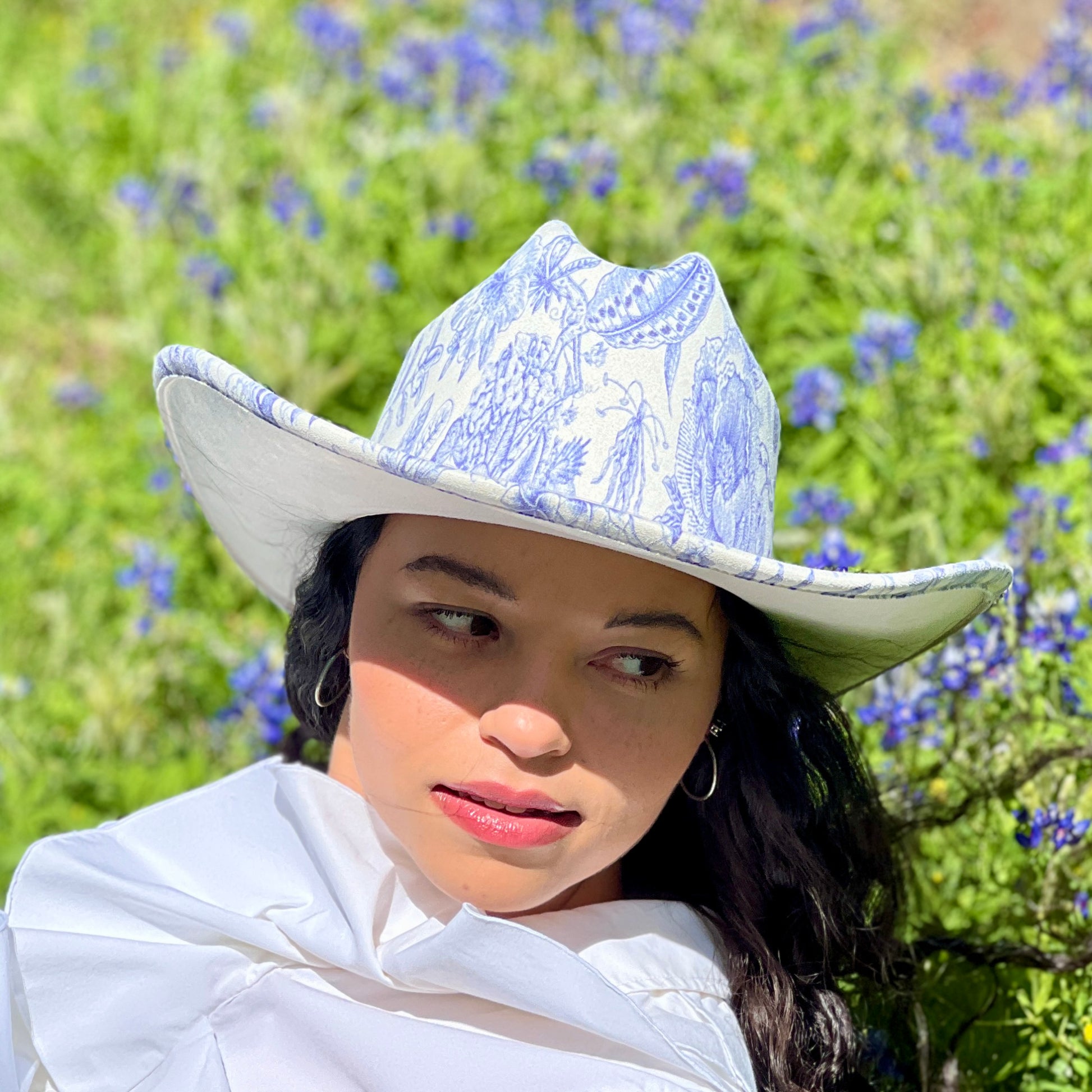 Person wearing a white cowboy hat with blue patterns in a field of flowers
