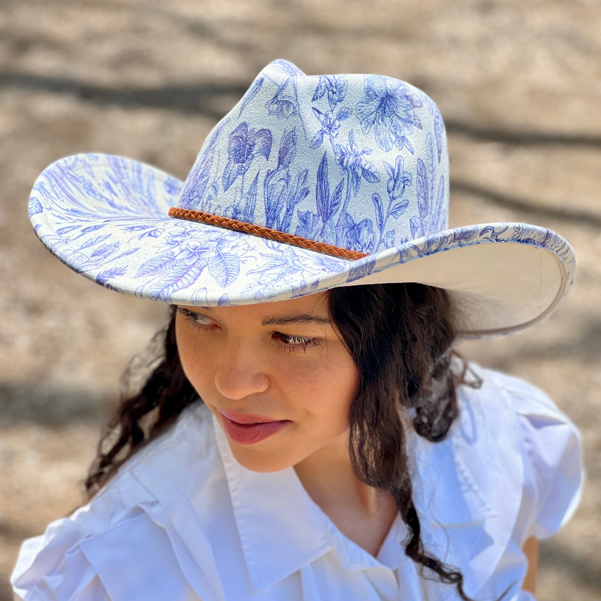 Woman wearing a blue floral-patterned hat and white shirt against a blurred background