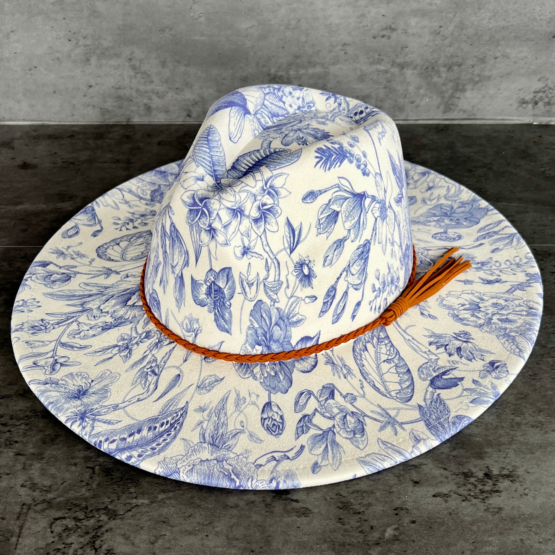 Floral-patterned sun hat with a brown band on a gray surface