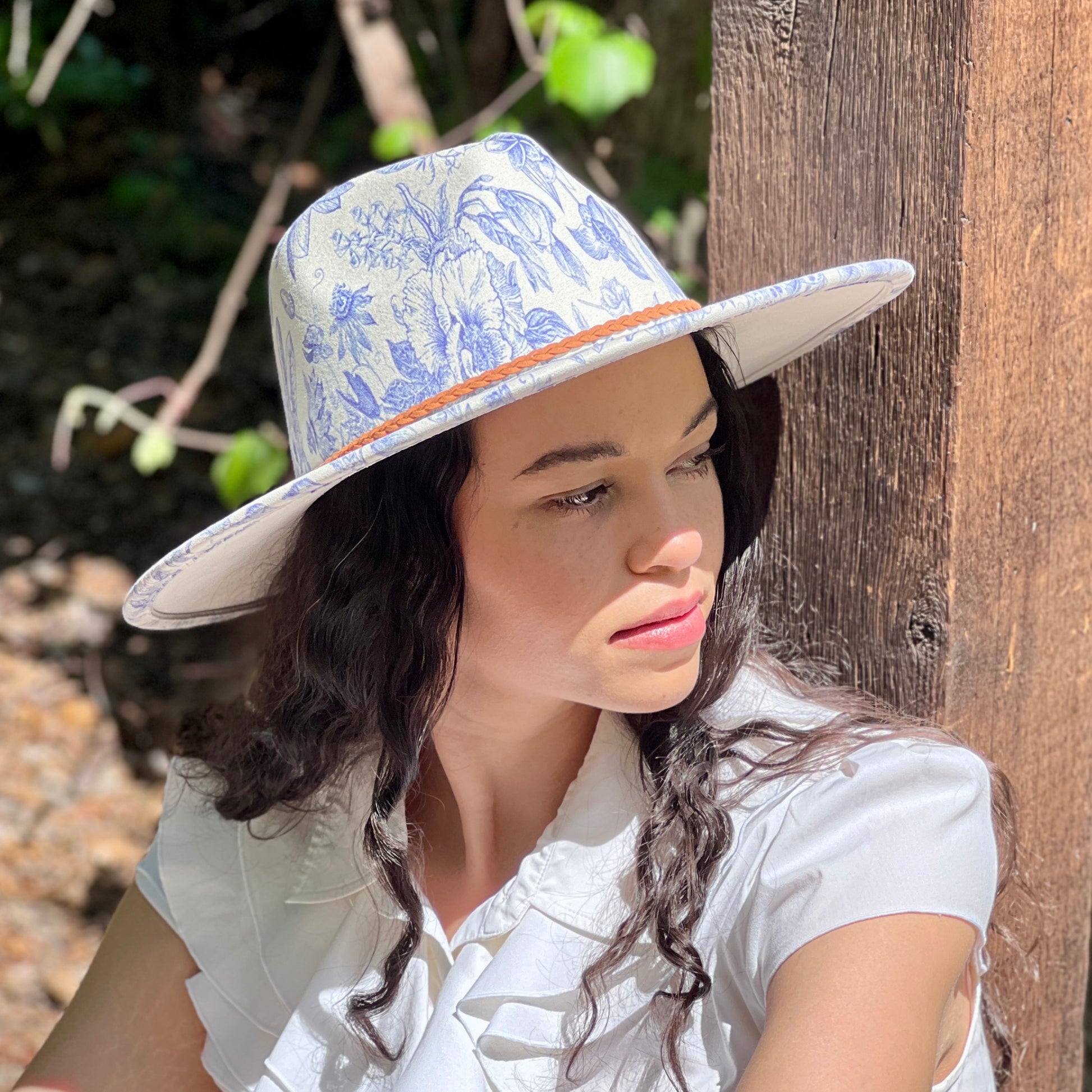 Woman wearing a floral hat leaning against a wooden post outdoors