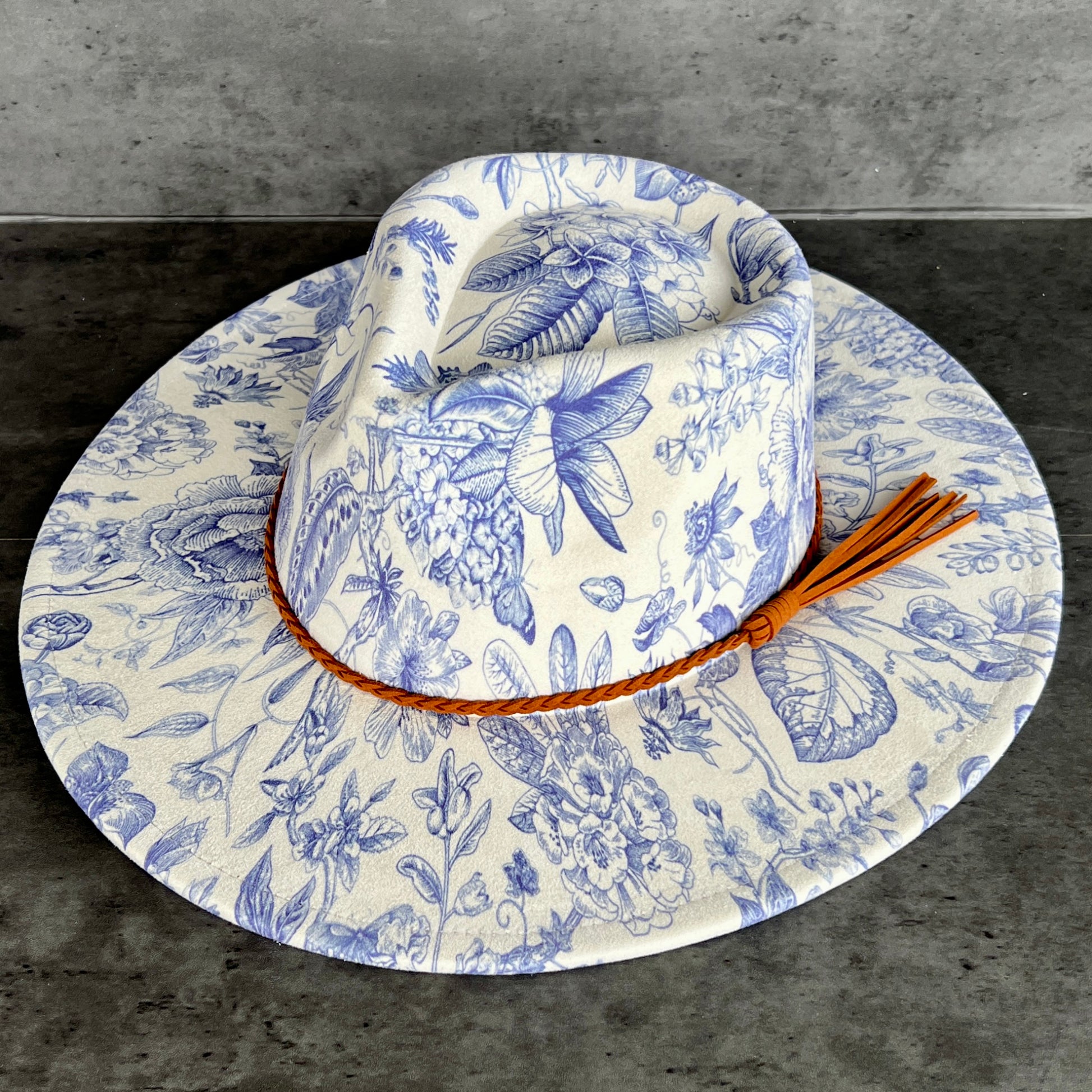 White cowboy hat with blue floral patterns and a brown leather band on a gray background