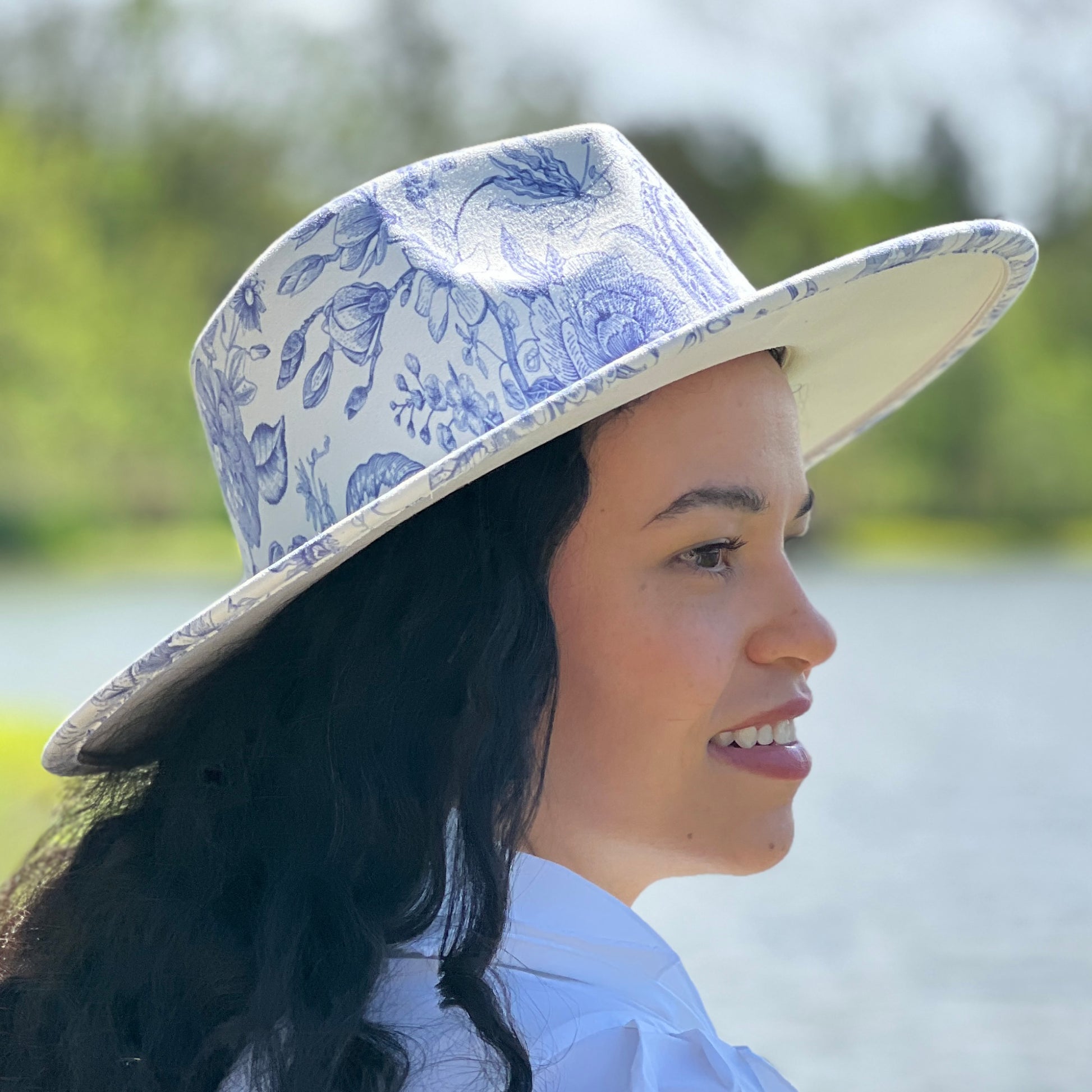 Woman wearing a blue floral-patterned hat outdoors by a body of water.
