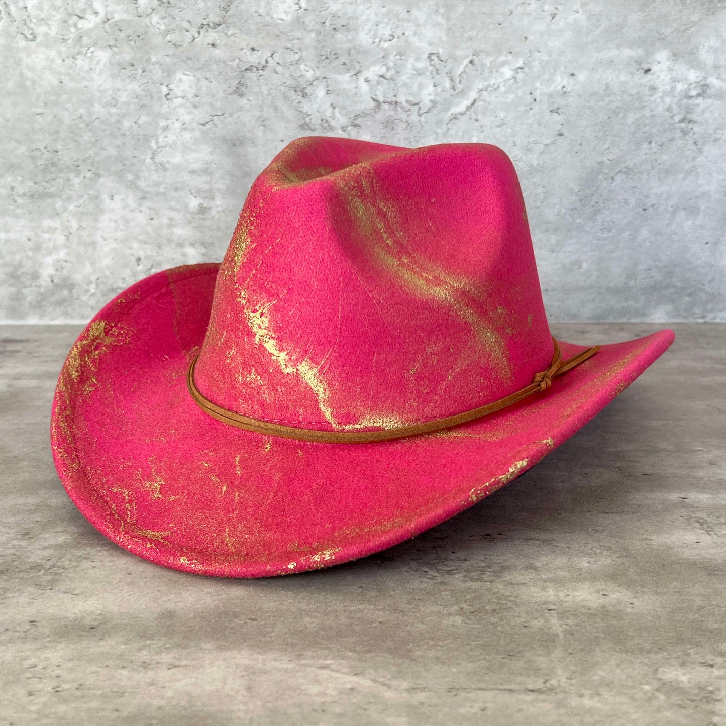 Hot pink fuchsia western cowboy hat painted with gold marbling. Has light brown faux suede cord hat band. 