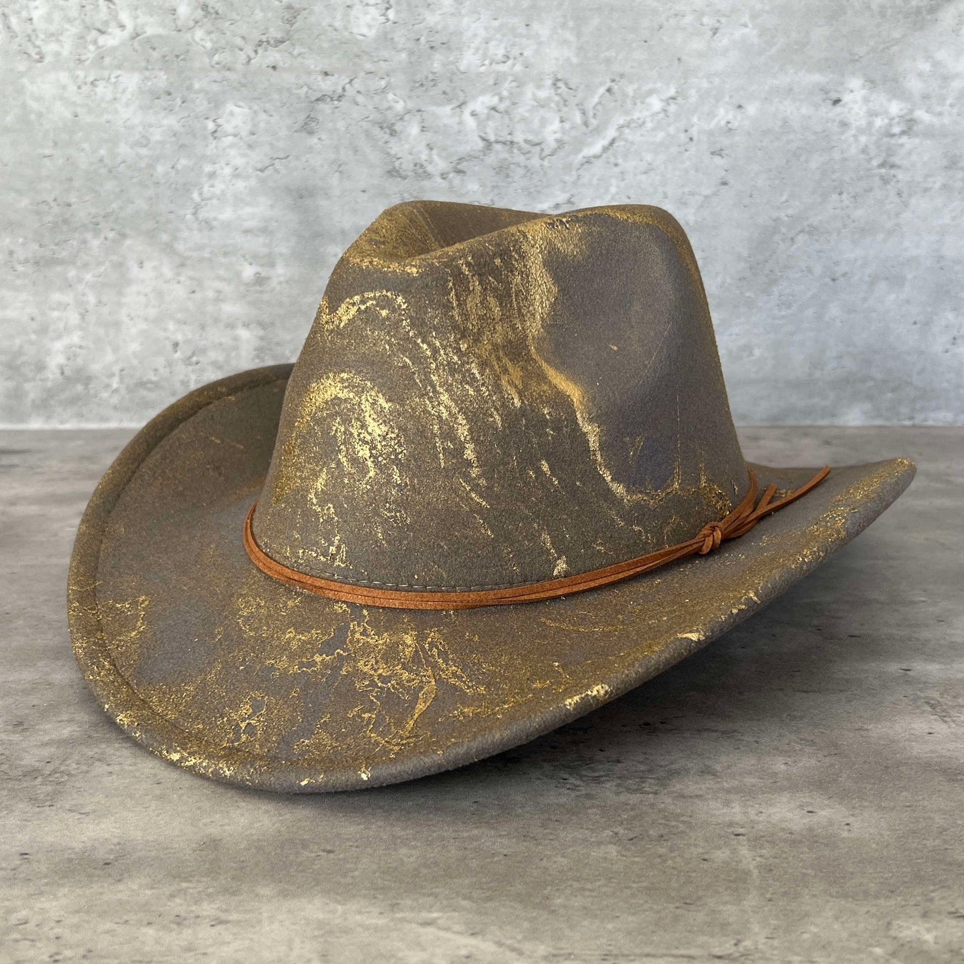 Light gray western cowboy hat painted with gold marbling. Has light brown faux suede cord hat band. 