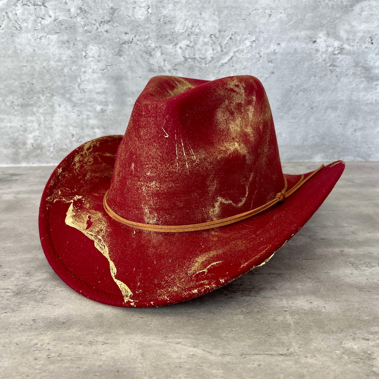 Maroon burgundy wine western cowboy hat painted with gold marbling. Has light brown faux suede cord hat band. 
