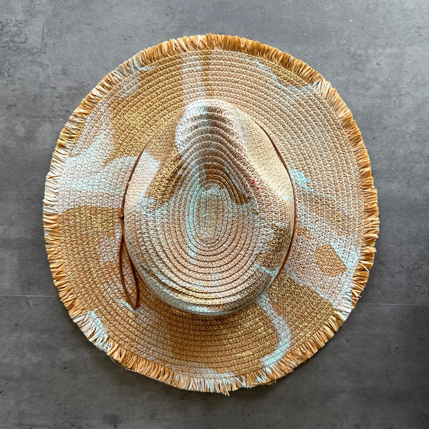 top view of tan khaki straw brim rancher hat with fringe has seafoam mint and gold paint marbling  and brown leather faux suede cord. sun hat.