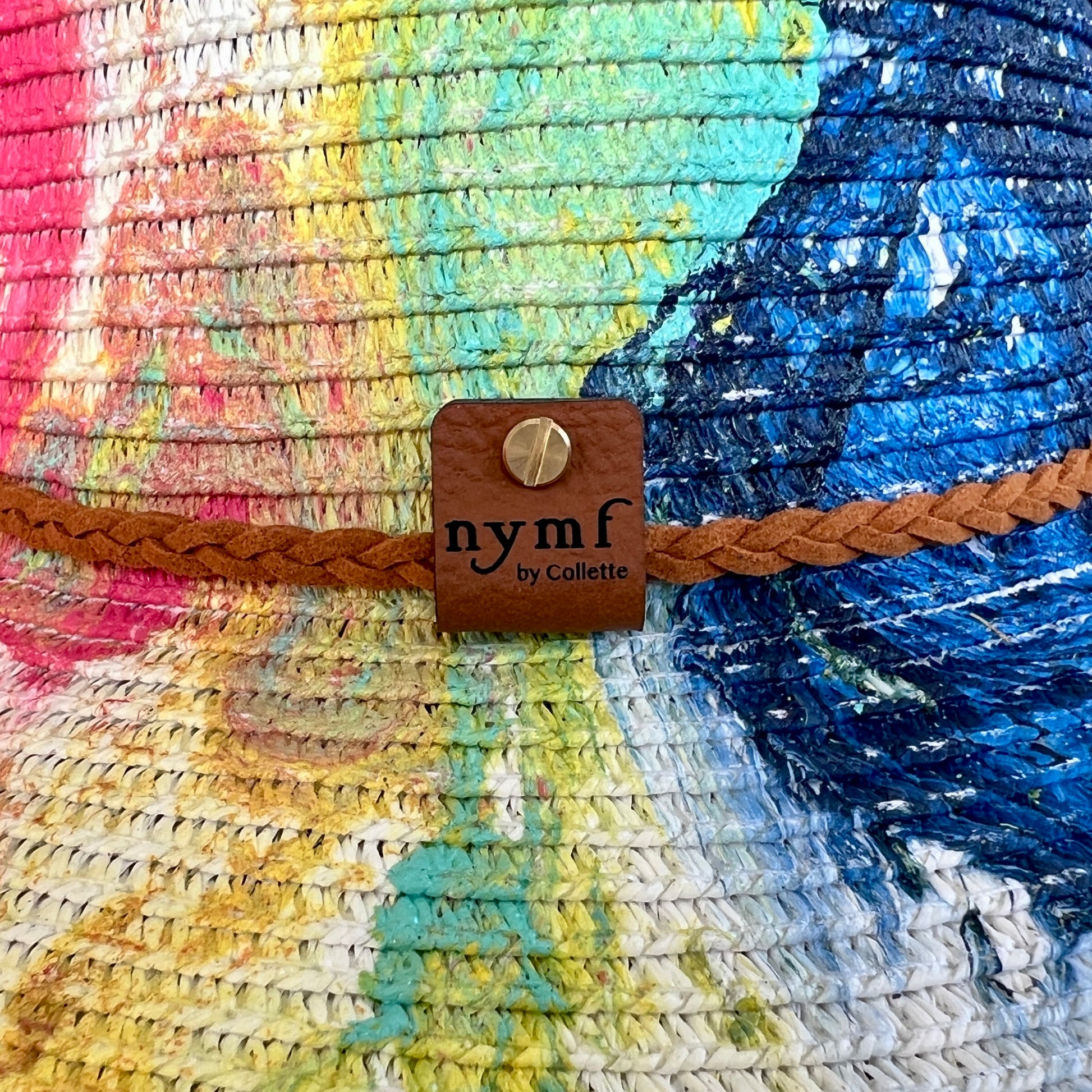 Colorful woven hat with a brown leather strap and 'nymf by Collette' label.
