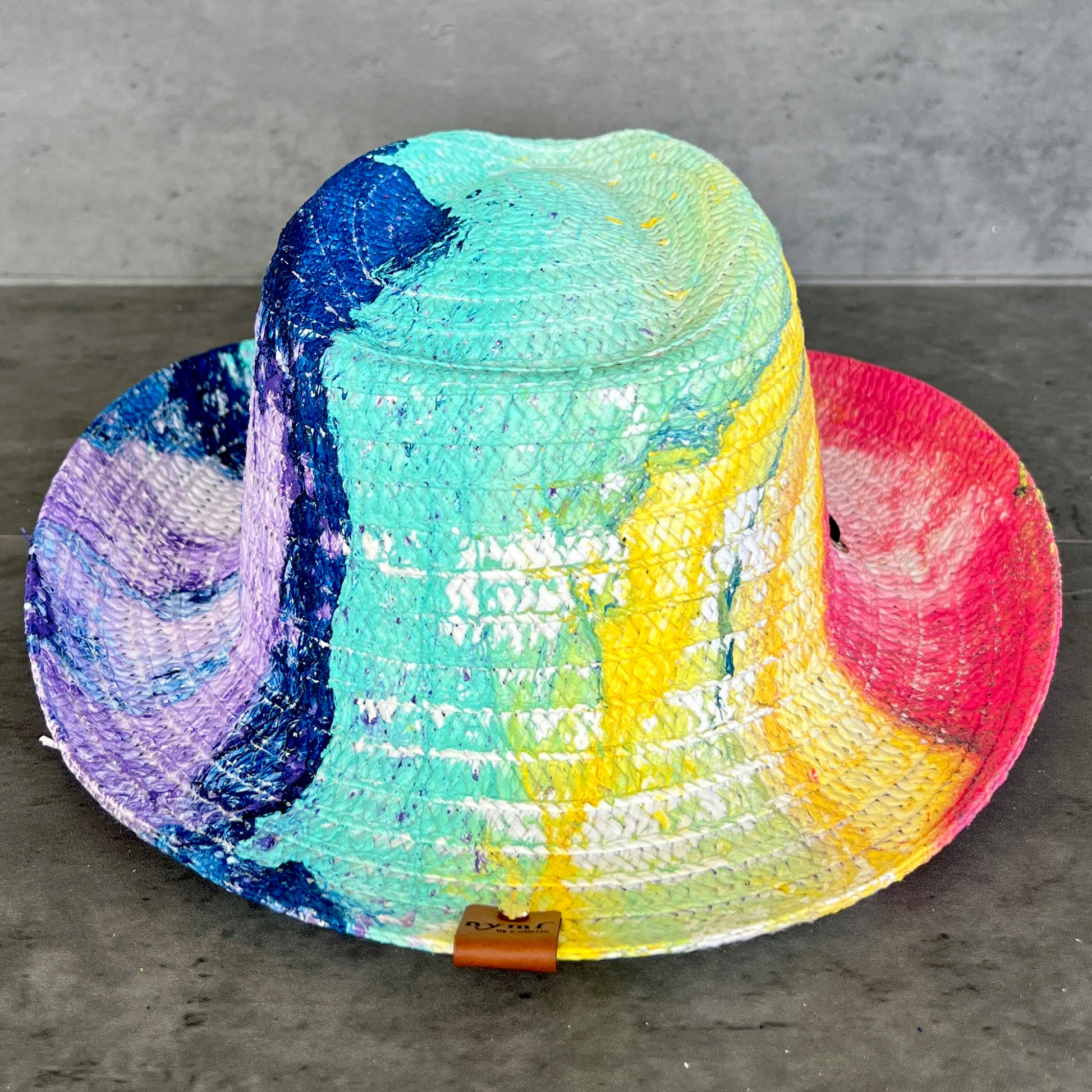 Colorful straw hat with a gradient of blue, green, yellow, and pink on a gray surface.