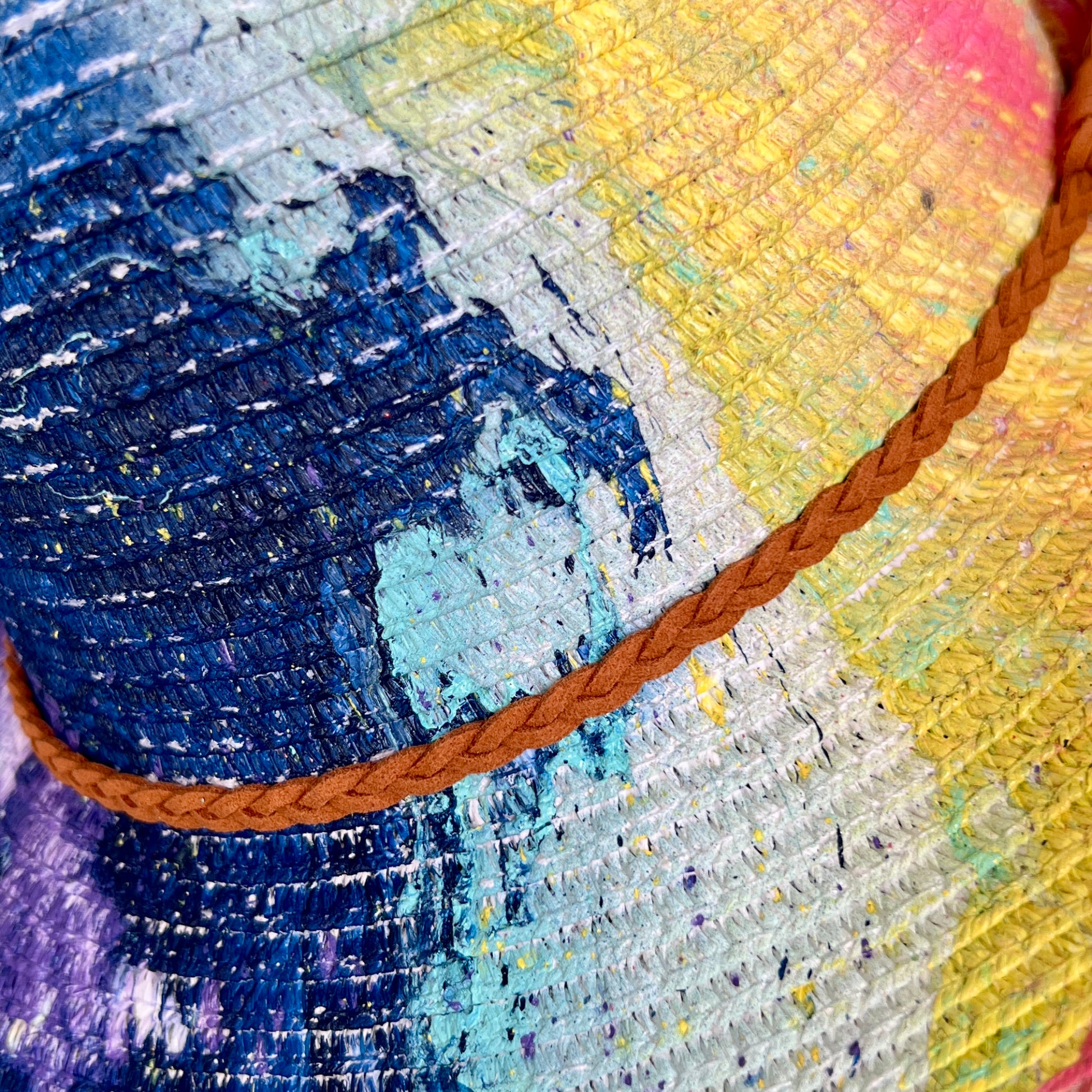Close-up of a straw hat with a brown cord, featuring blue, yellow, and purple colors.