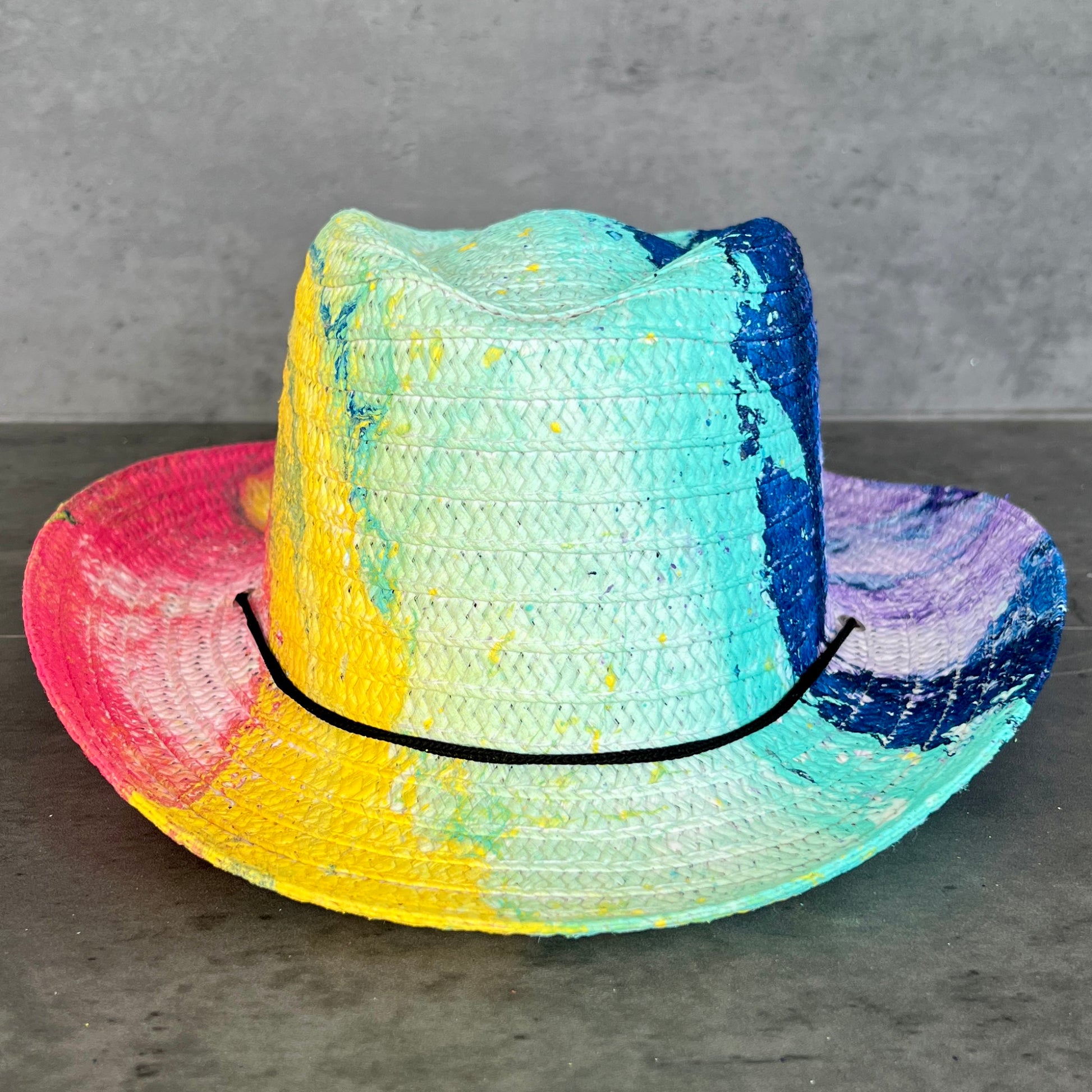 Colorful straw hat with a gradient of pink, yellow, blue, and green on a gray surface.