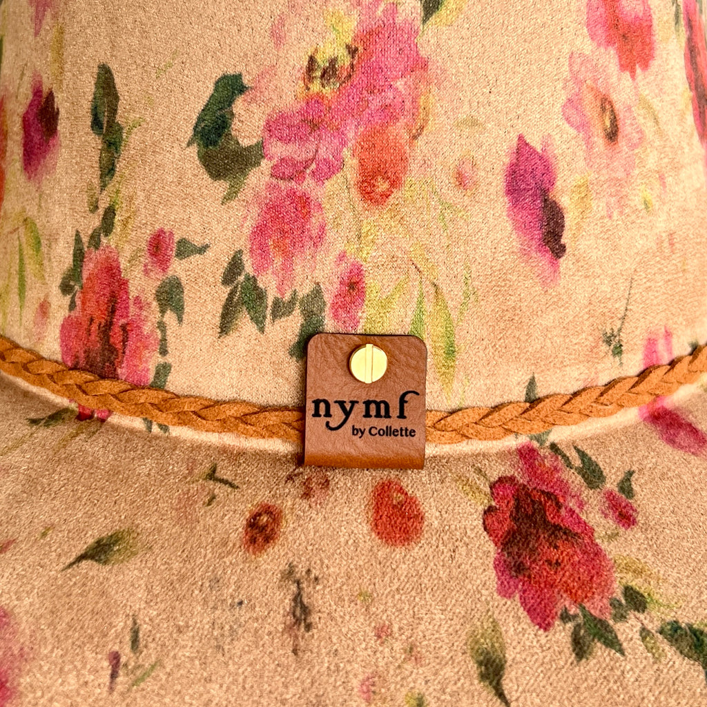 Close-up of a tan hat with pink and red flowers, green leaves, and a braided tan rope trim. 