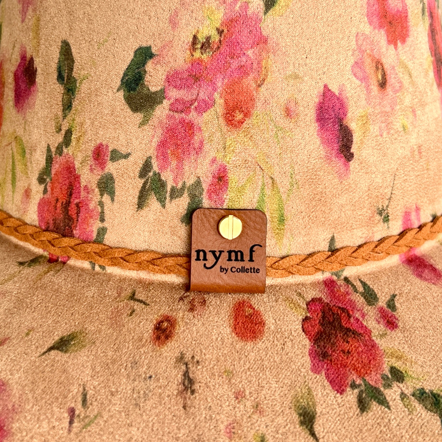 Close-up of a tan hat with pink and red flowers, green leaves, and a braided tan rope trim. 