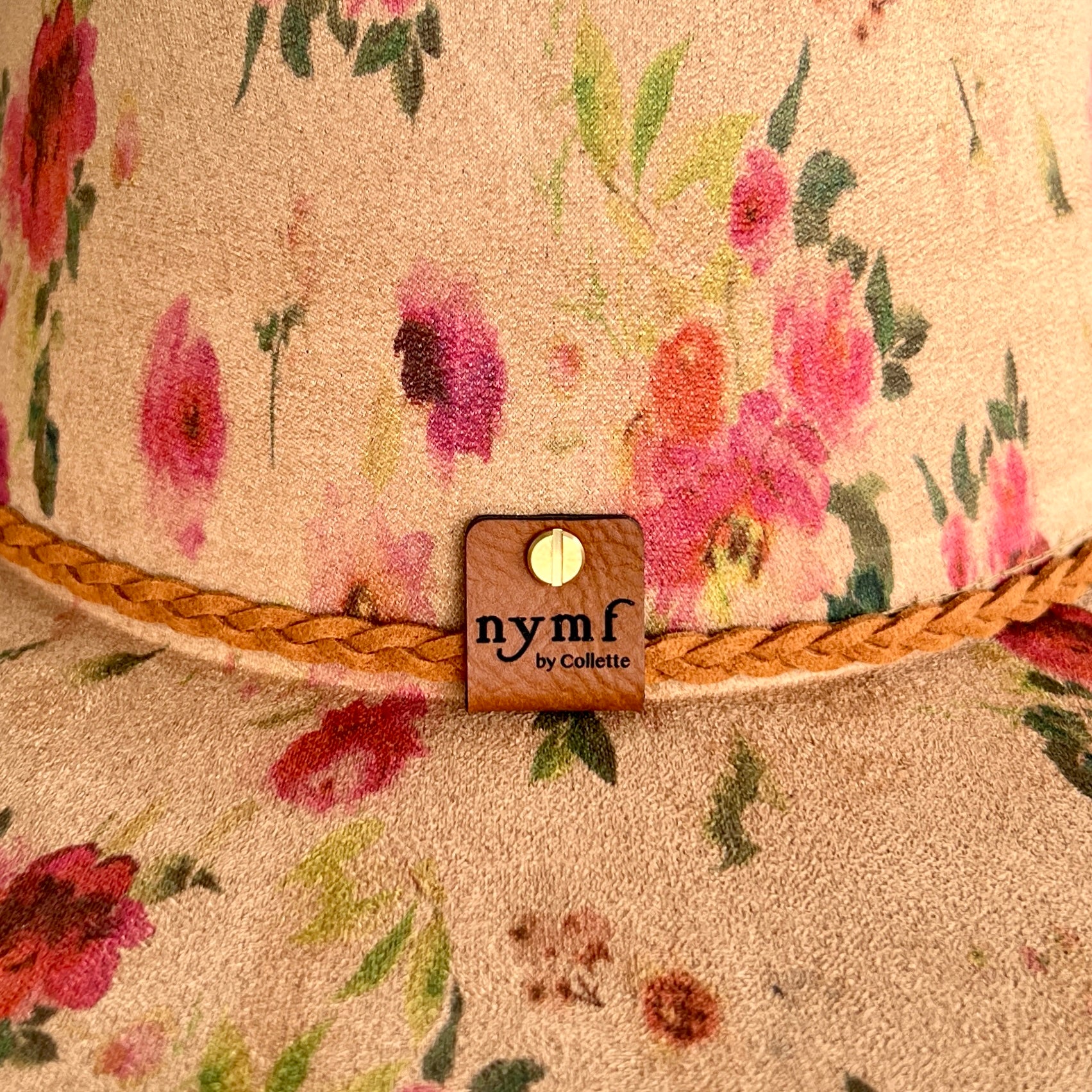 Close-up of a floral rancher hat with pink and red flowers on a tan background, featuring a braided tan rope detail