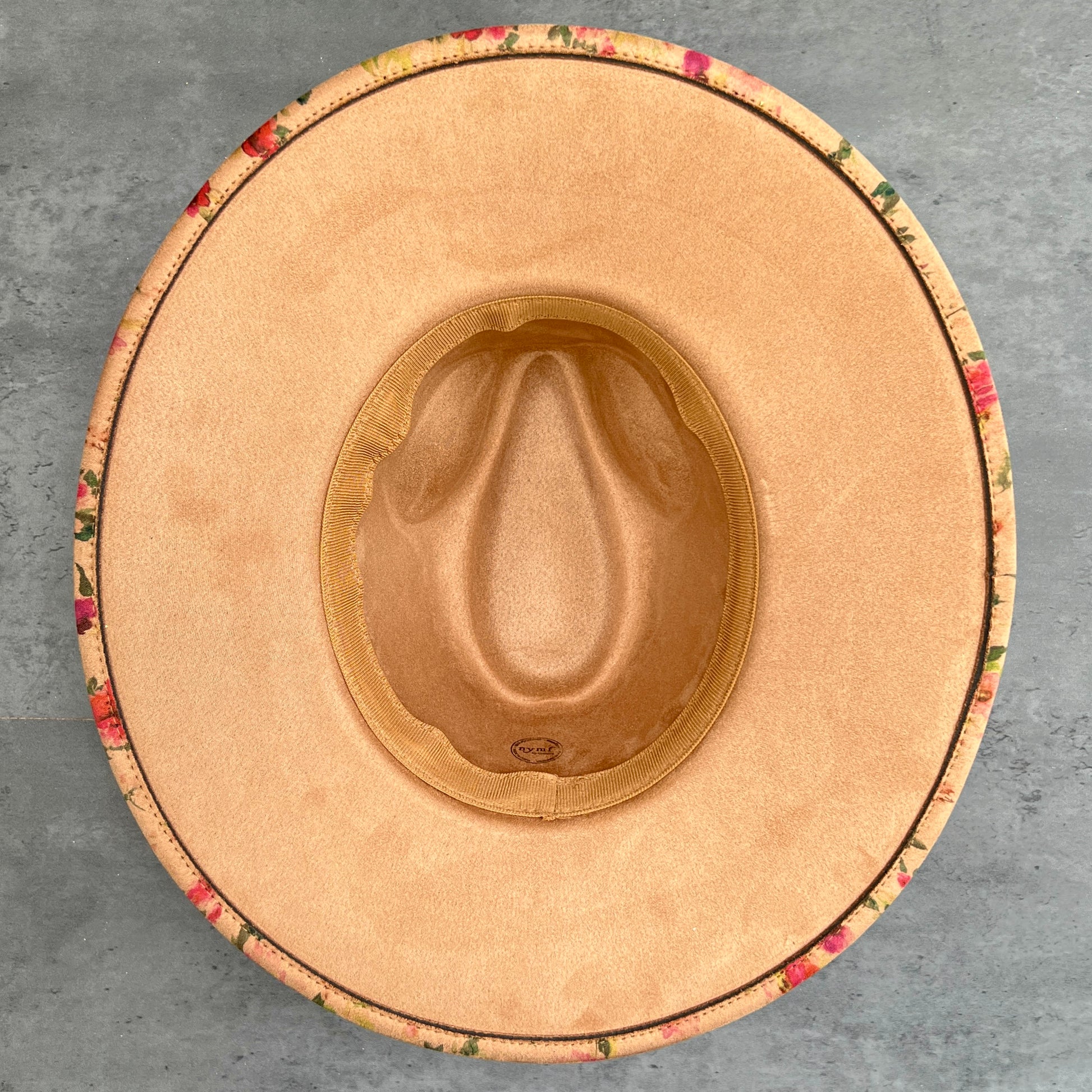 Top-down view of a rancher hat underside with a tan suede set against a gray concrete background.