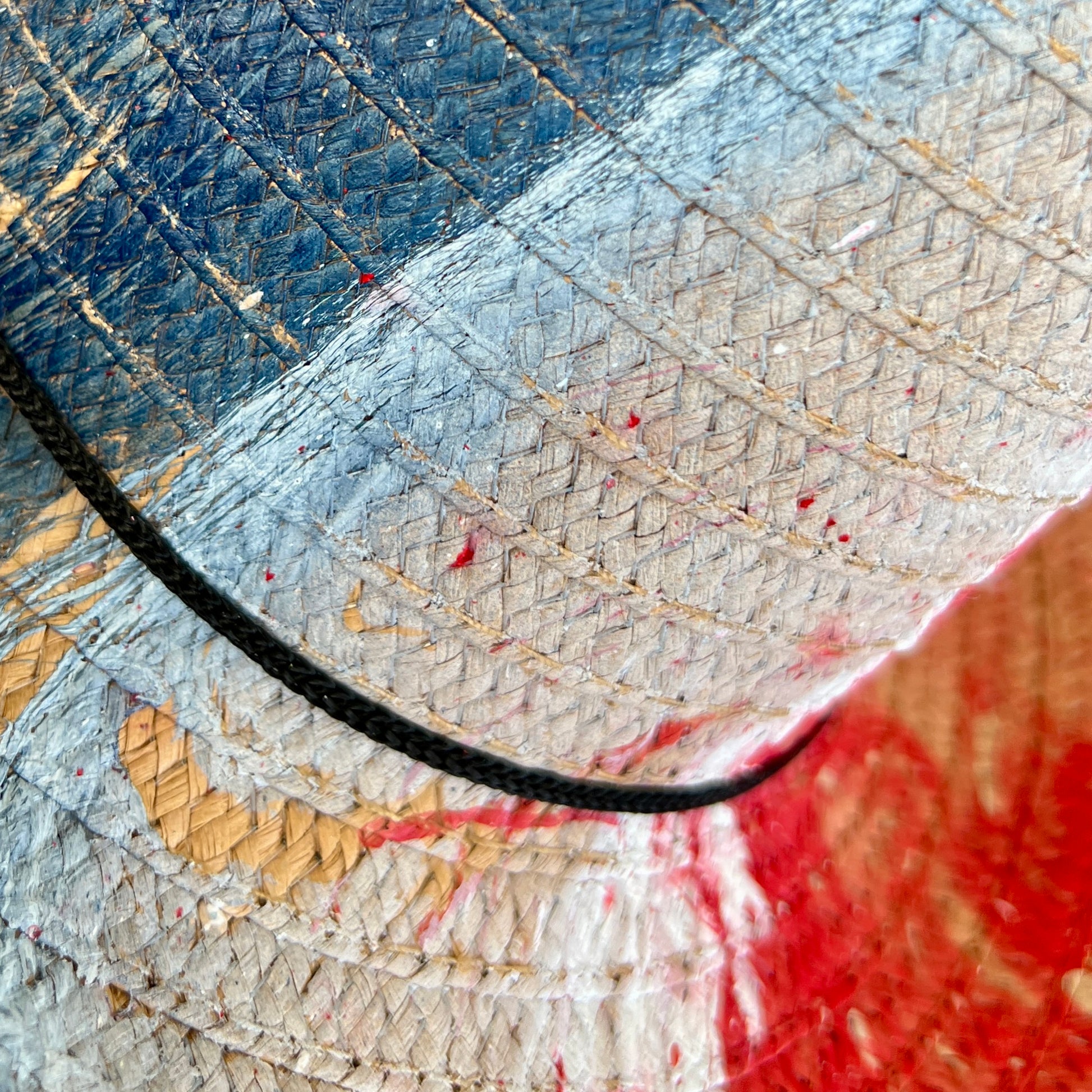 Close-up of a straw hat with a black cord and red paint splatter.