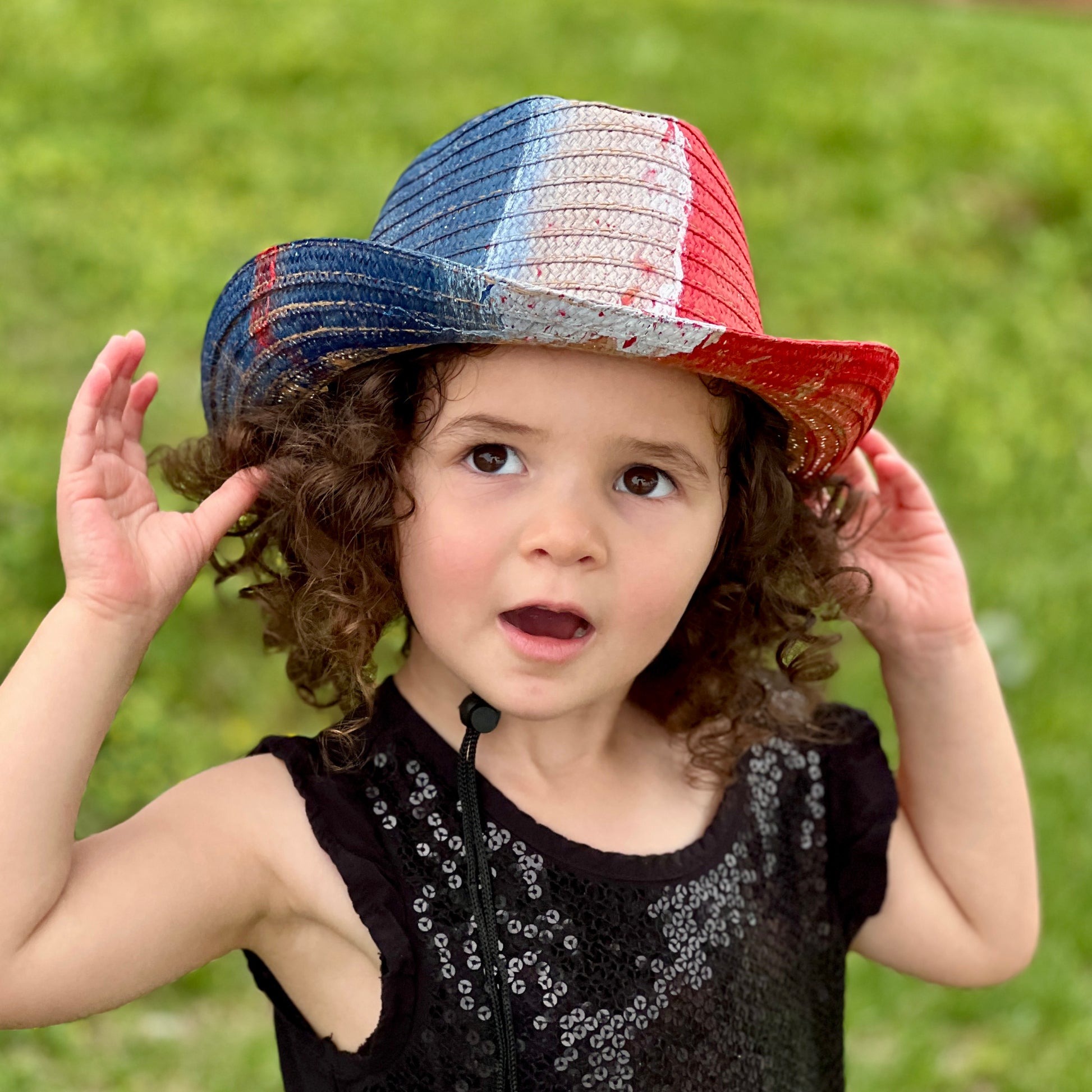 Child wearing a colorful straw hat outdoors on a grassy background