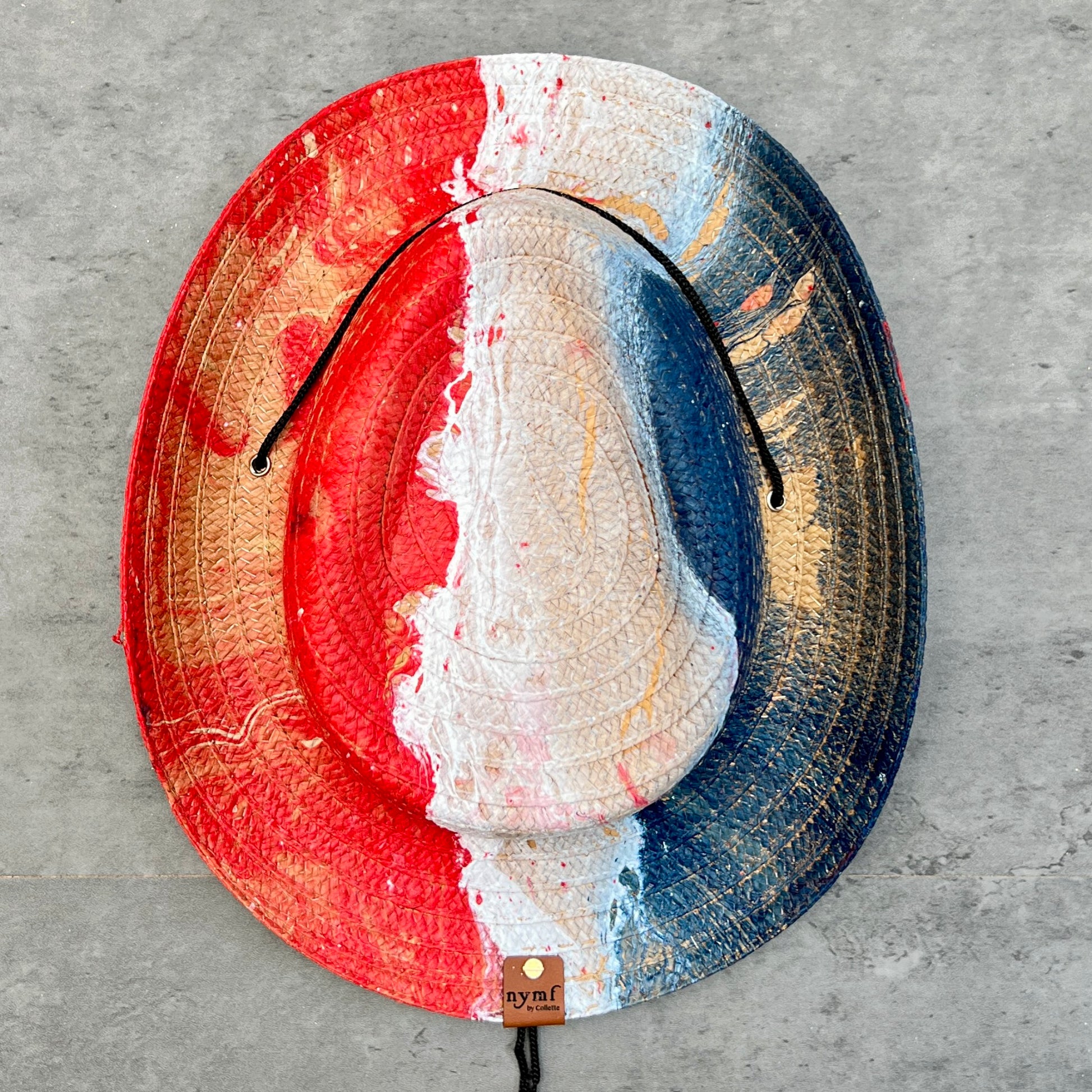 Colorful straw hat with a brand tag on a gray concrete surface
