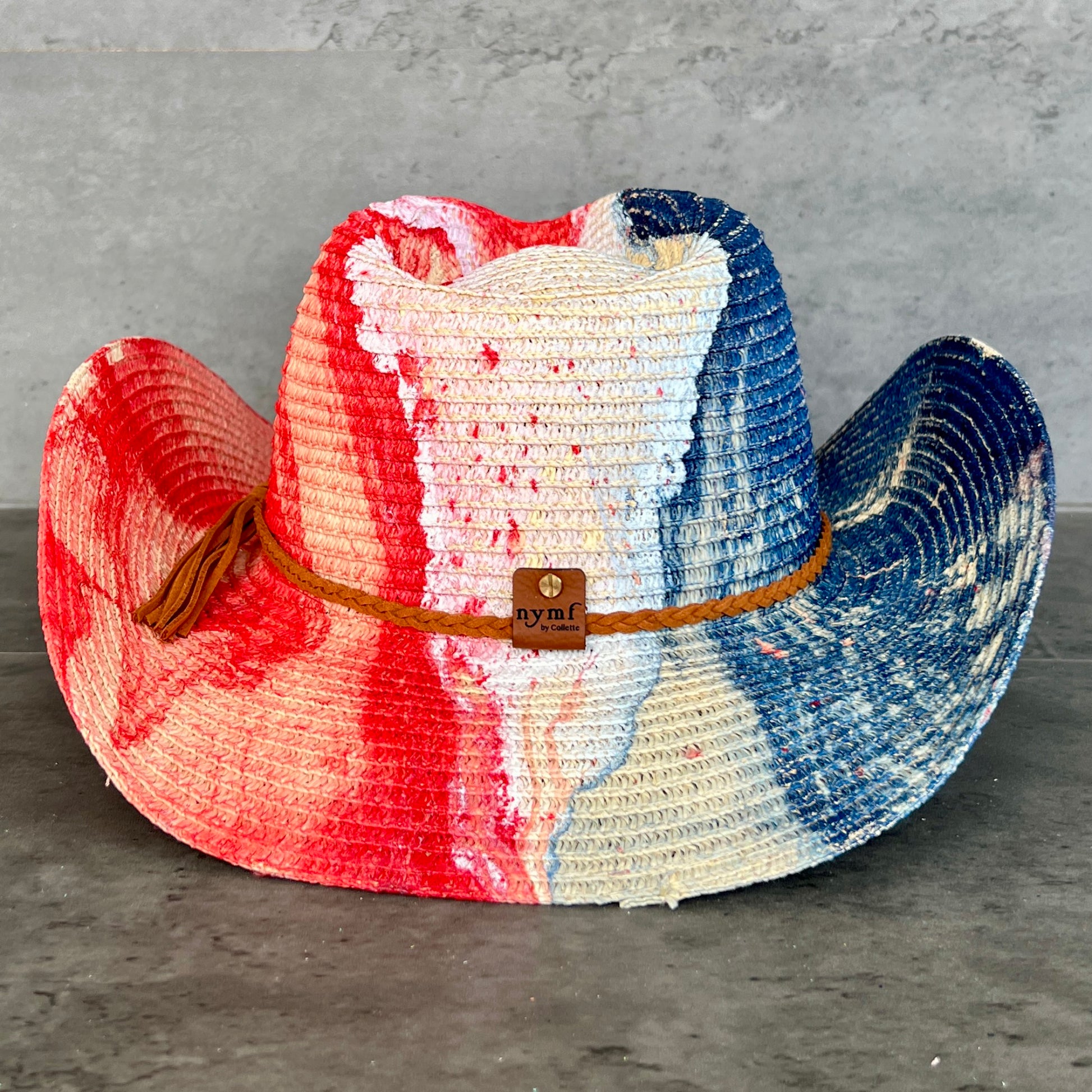 Colorful red white and blue straw cowboy hat with a brown band on a gray surface
