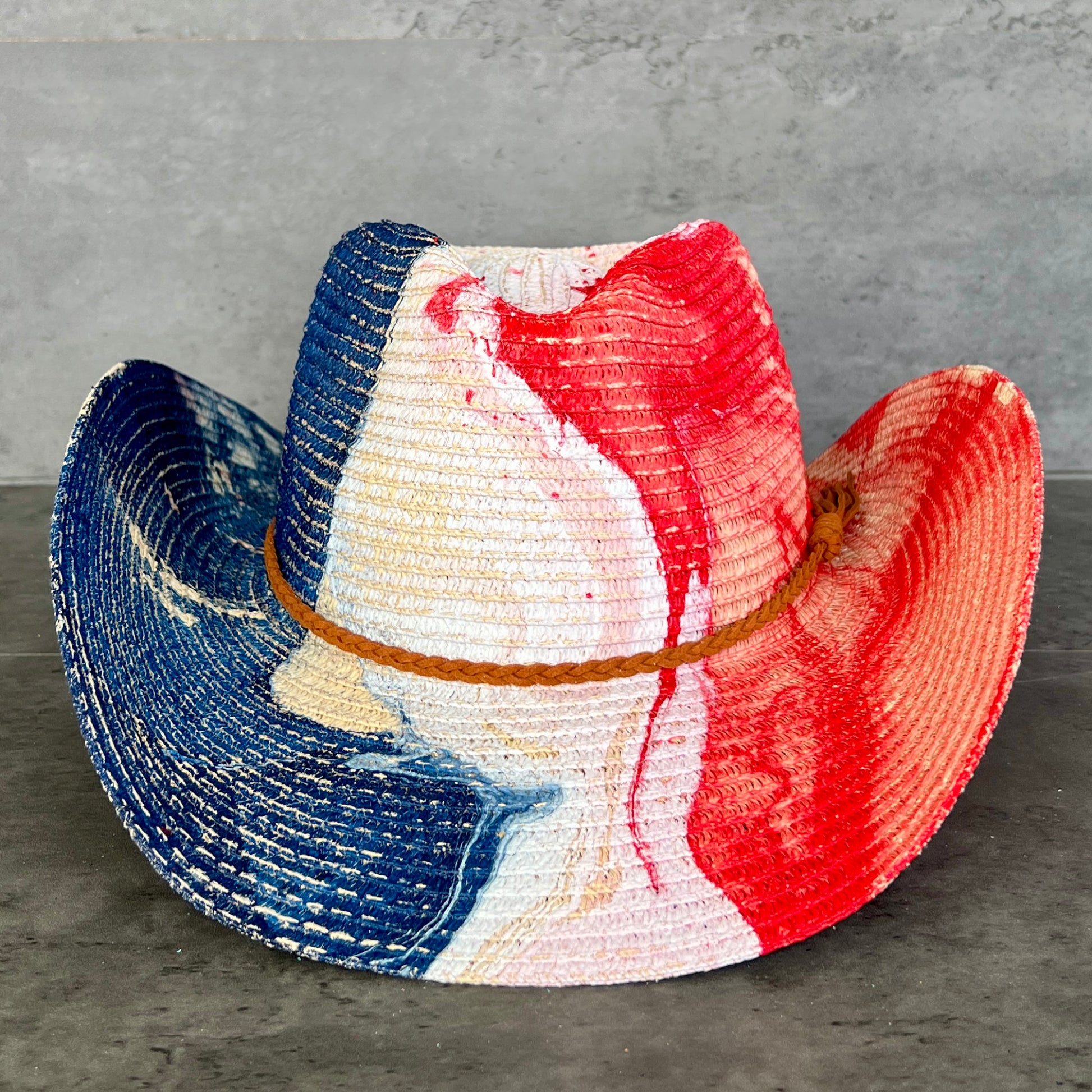 Colorful straw cowboy hat with blue, red, and white stripes on a gray surface.