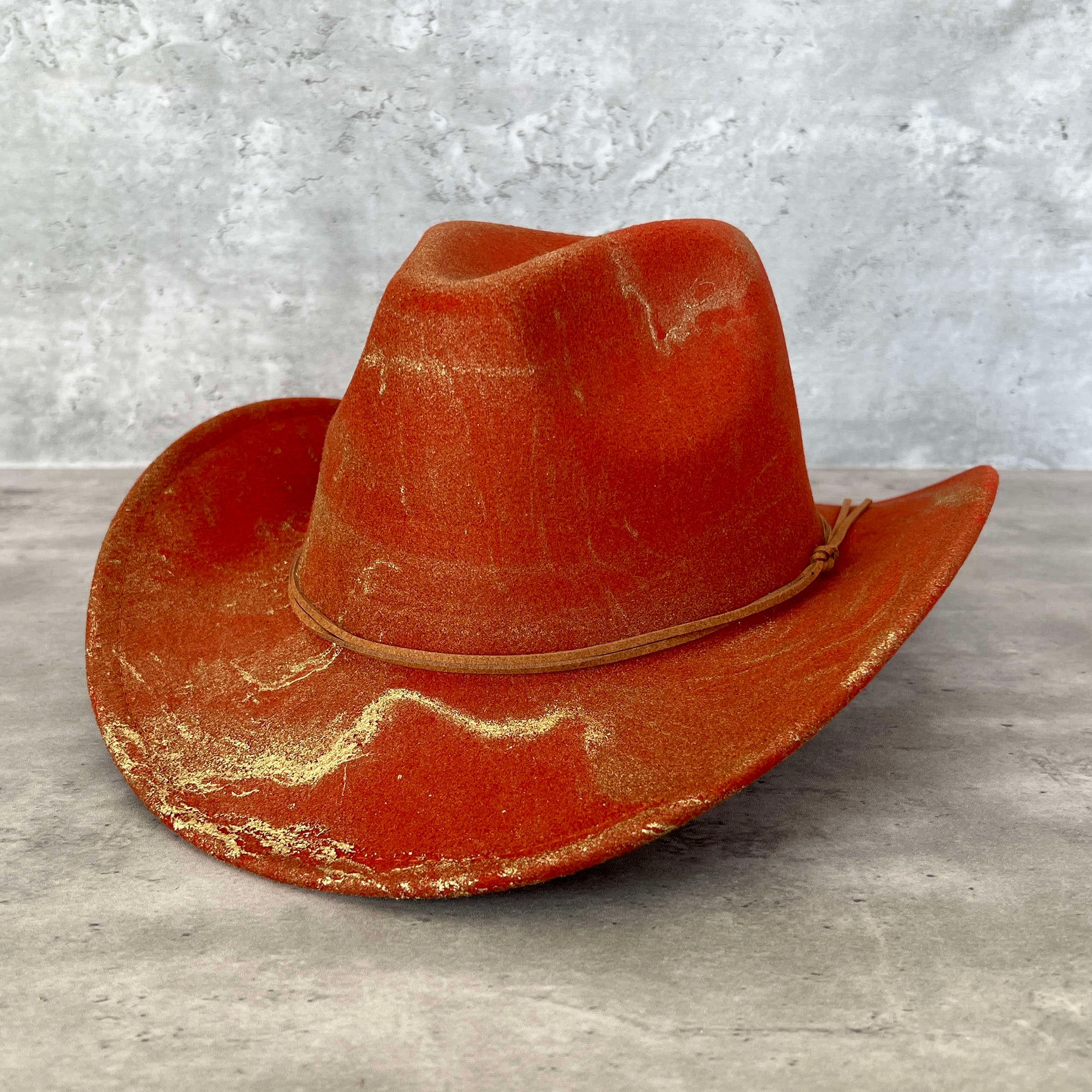 Rust burnt orange UT western cowboy hat painted with gold marbling. Has light brown faux suede cord hat band. 