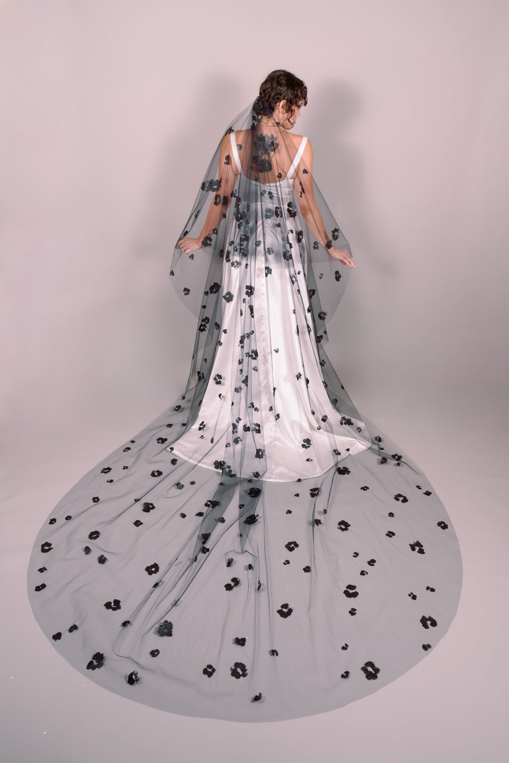 Woman wearing a wedding dress and black veil with painted black floral petals on a plain background. Photography by Rachel Sakakeeny Model is Isabelle Paulino