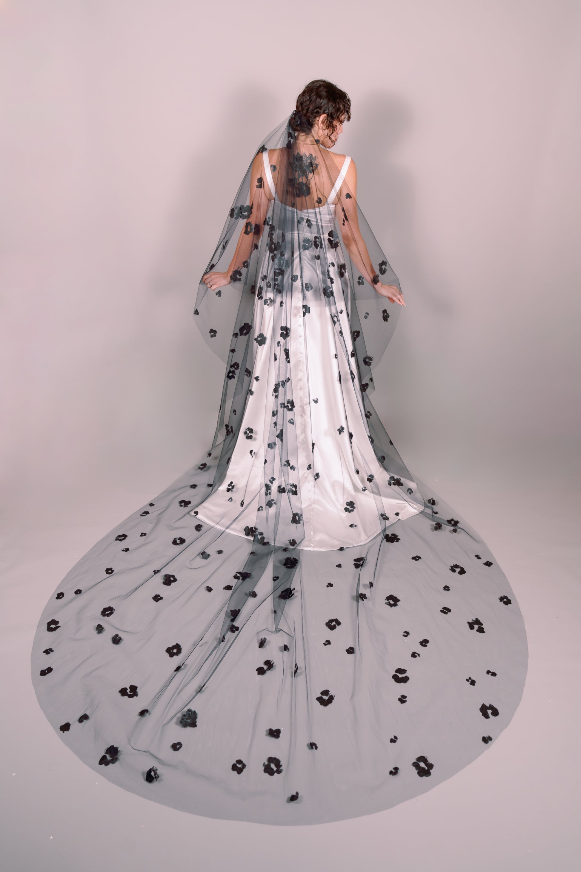 Woman wearing a wedding dress and black veil with painted black floral petals on a plain background. Photography by Rachel Sakakeeny Model is Isabelle Paulino