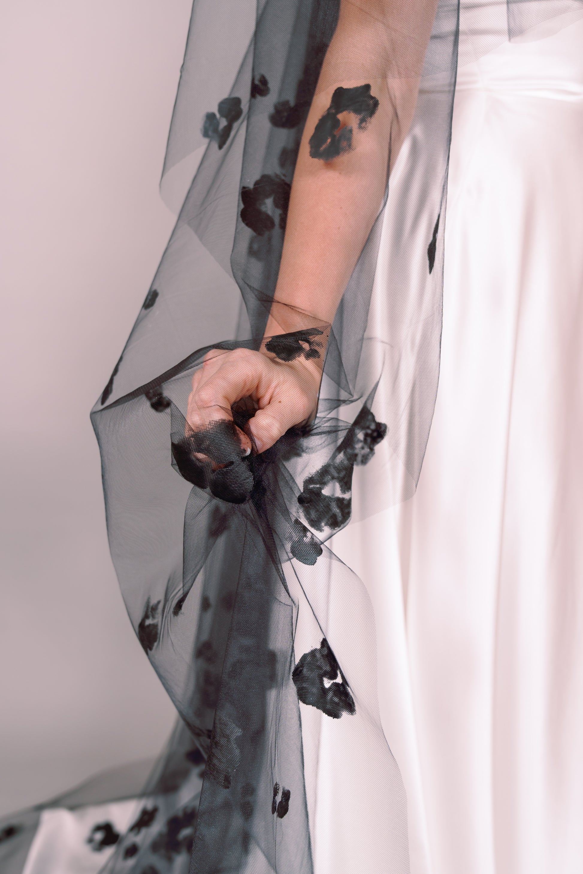 Woman wearing a wedding dress and black veil with painted black floral petals on a plain background. Photography by Rachel Sakakeeny Model is Isabelle Paulino