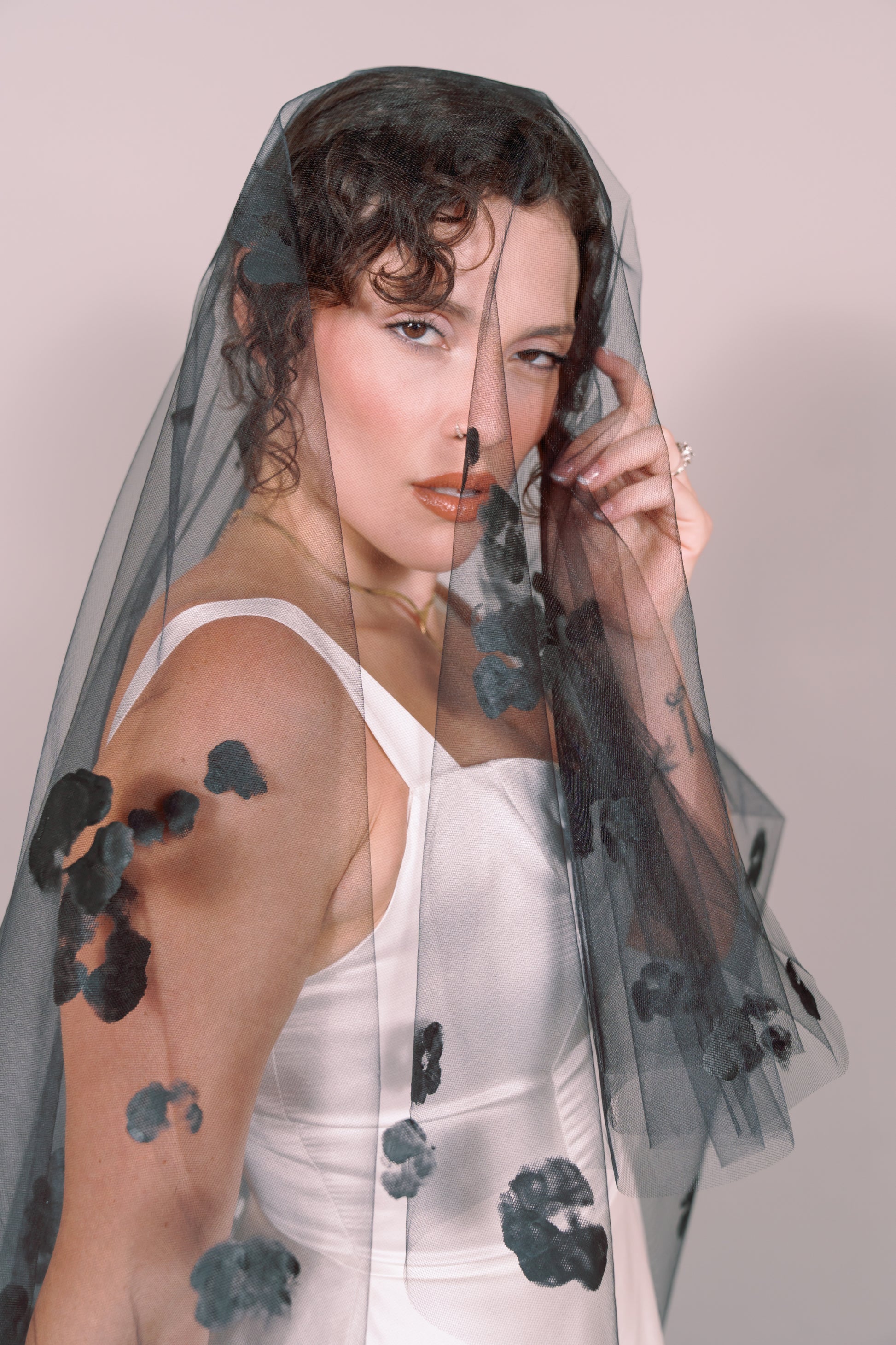 Woman wearing a wedding dress and black veil with painted black floral petals on a plain background. Photography by Rachel Sakakeeny Model is Isabelle Paulino