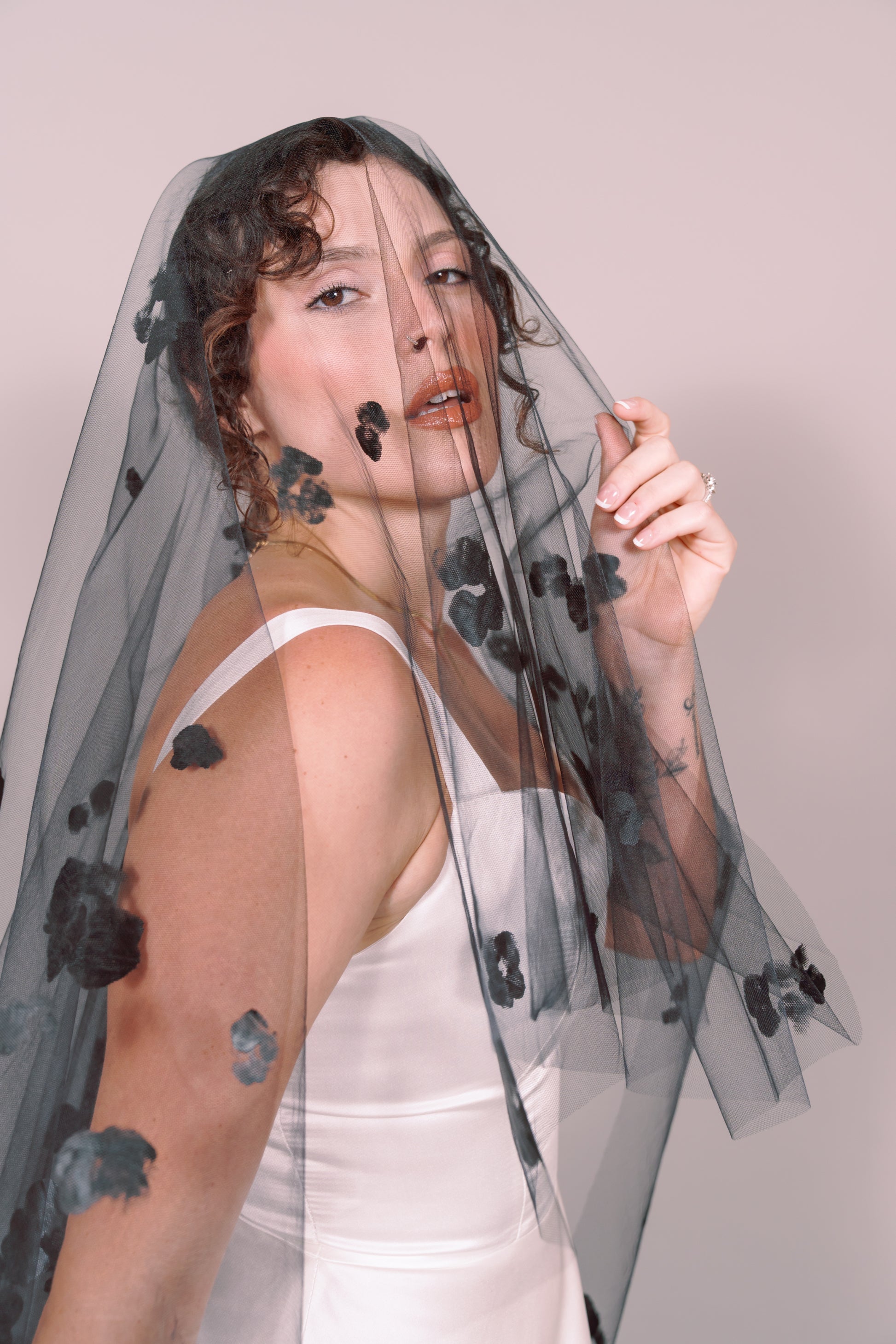 Woman wearing a wedding dress and black veil with painted black floral petals on a plain background. Photography by Rachel Sakakeeny Model is Isabelle Paulino