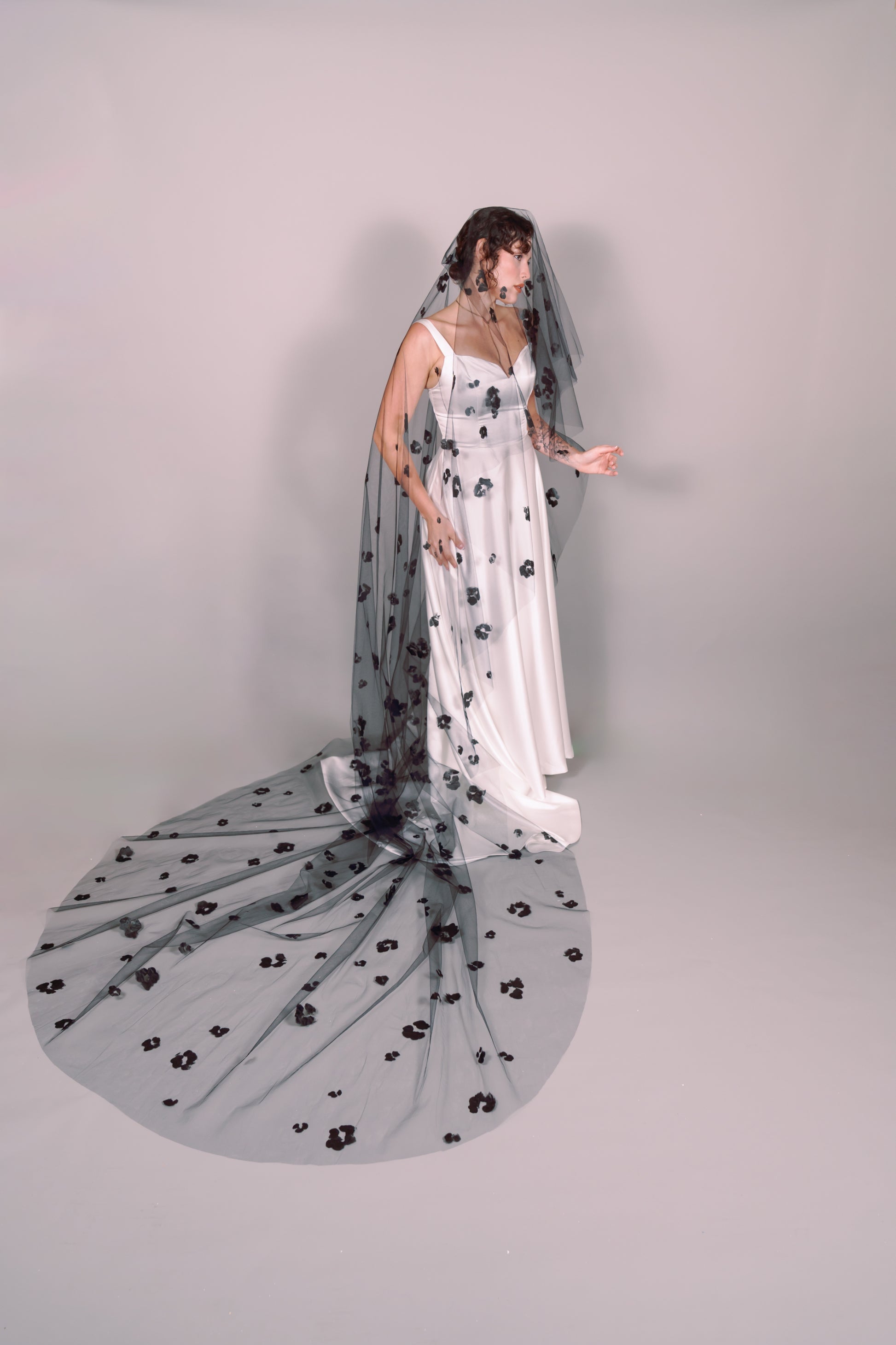 Woman wearing a wedding dress and black veil with painted black floral petals on a plain background. Photography by Rachel Sakakeeny Model is Isabelle Paulino