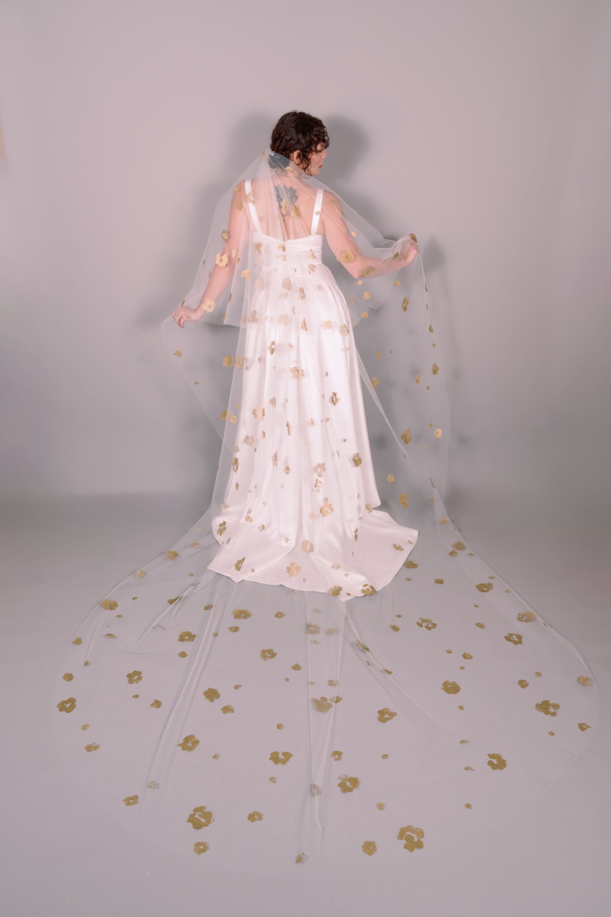 Woman wearing a wedding dress  and ivory veil with painted gold floral petals on a plain background. Photography by Rachel Sakakeeny Model is Isabelle Paulino