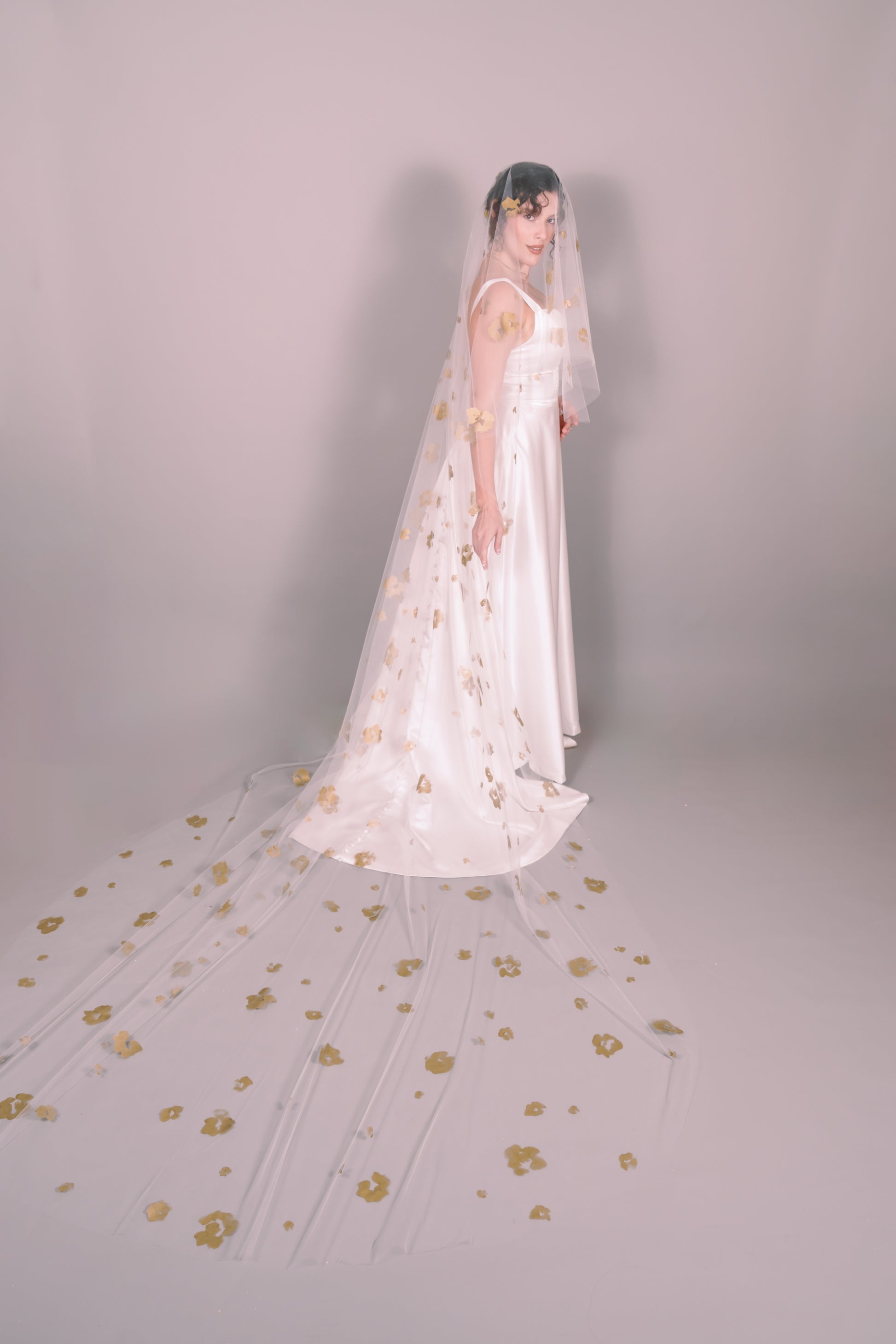 Woman wearing a wedding dress and ivory veil with painted gold floral petals on a plain background. Photography by Rachel Sakakeeny Model is Isabelle Paulino