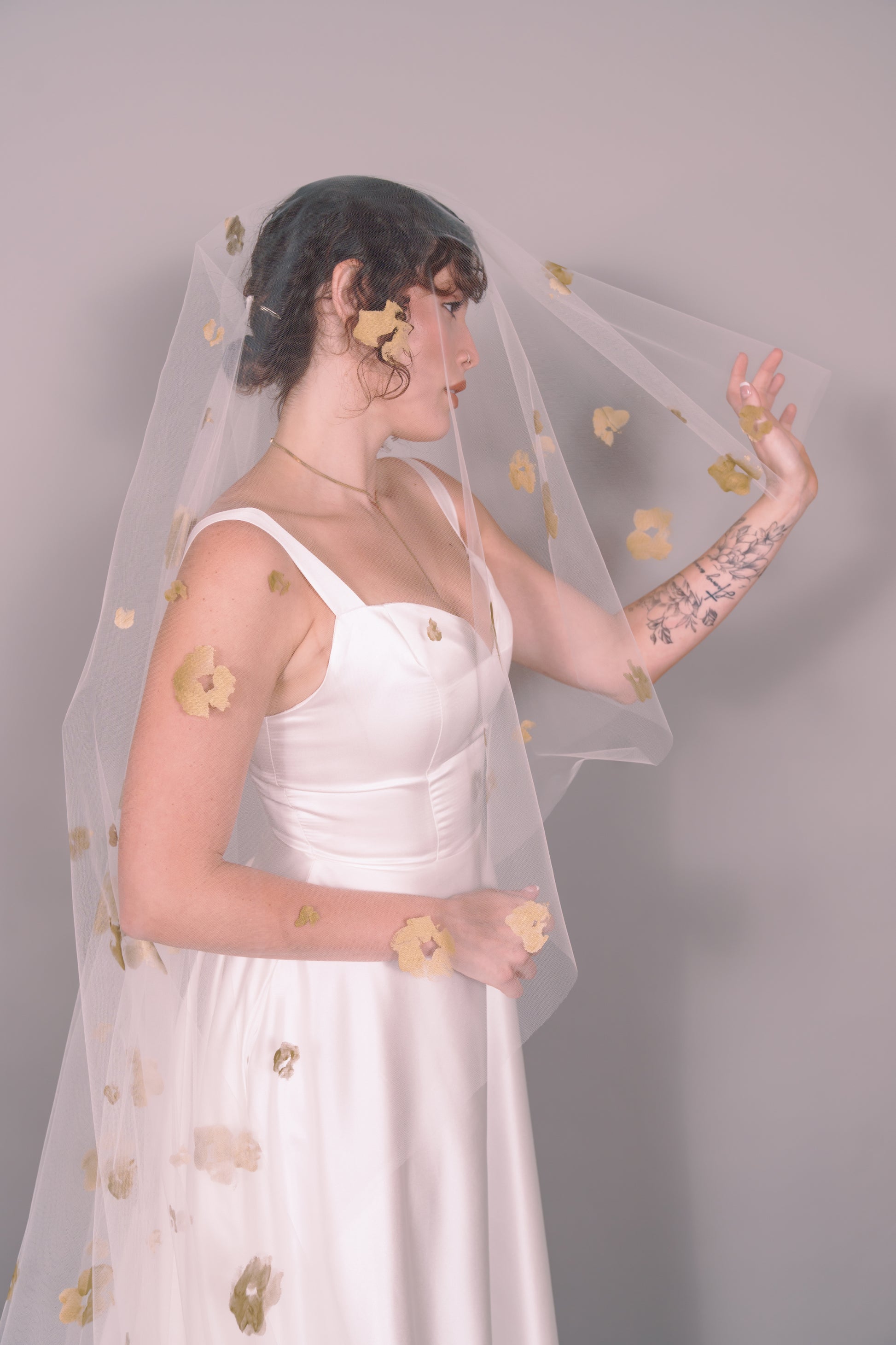 Woman wearing a wedding dress and ivory veil with painted gold floral petals on a plain background. Photography by Rachel Sakakeeny Model is Isabelle Paulino