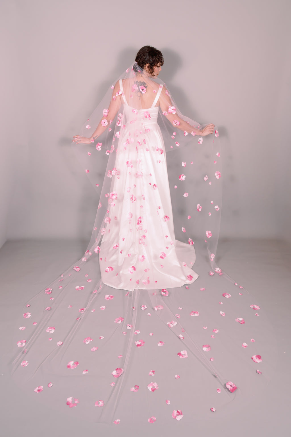 Woman wearing a wedding dress and pink veil with painted pink floral petals on a plain background. Photography by Rachel Sakakeeny Model is Isabelle Paulino