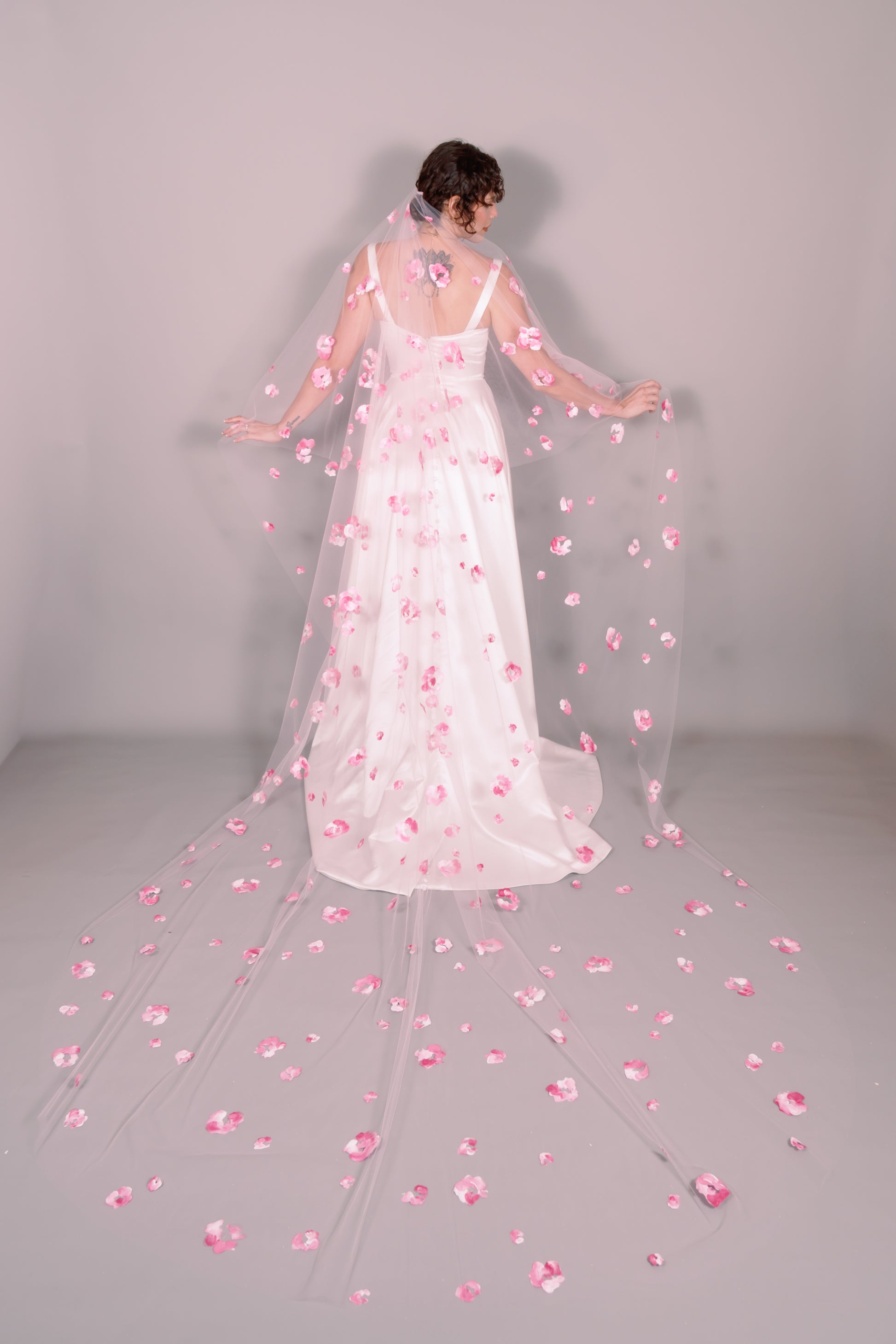 Woman wearing a wedding dress and pink veil with painted pink floral petals on a plain background. Photography by Rachel Sakakeeny Model is Isabelle Paulino