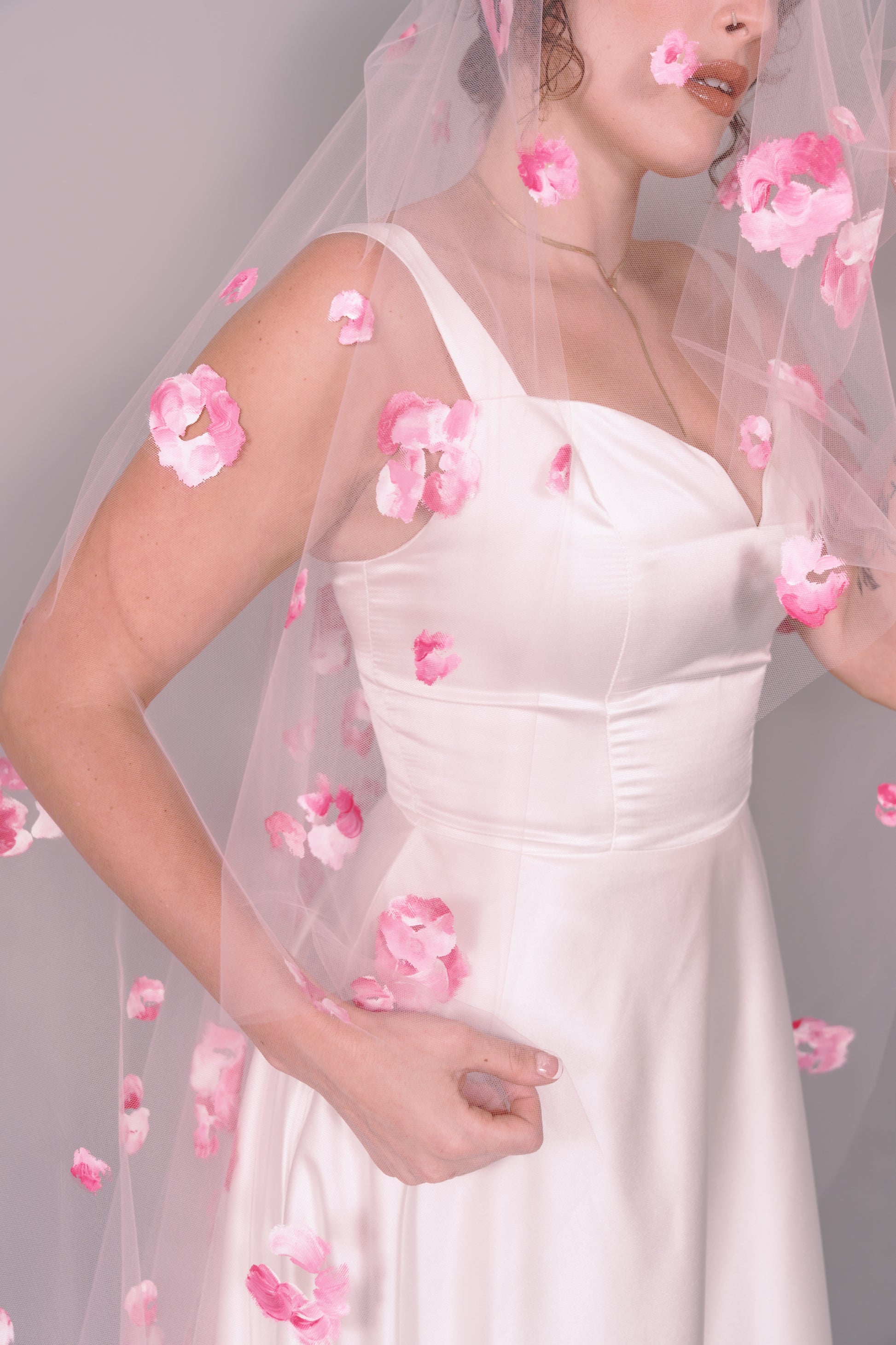 Woman wearing a wedding dress and pink veil with painted pink floral petals on a plain background. Photography by Rachel Sakakeeny Model is Isabelle Paulino