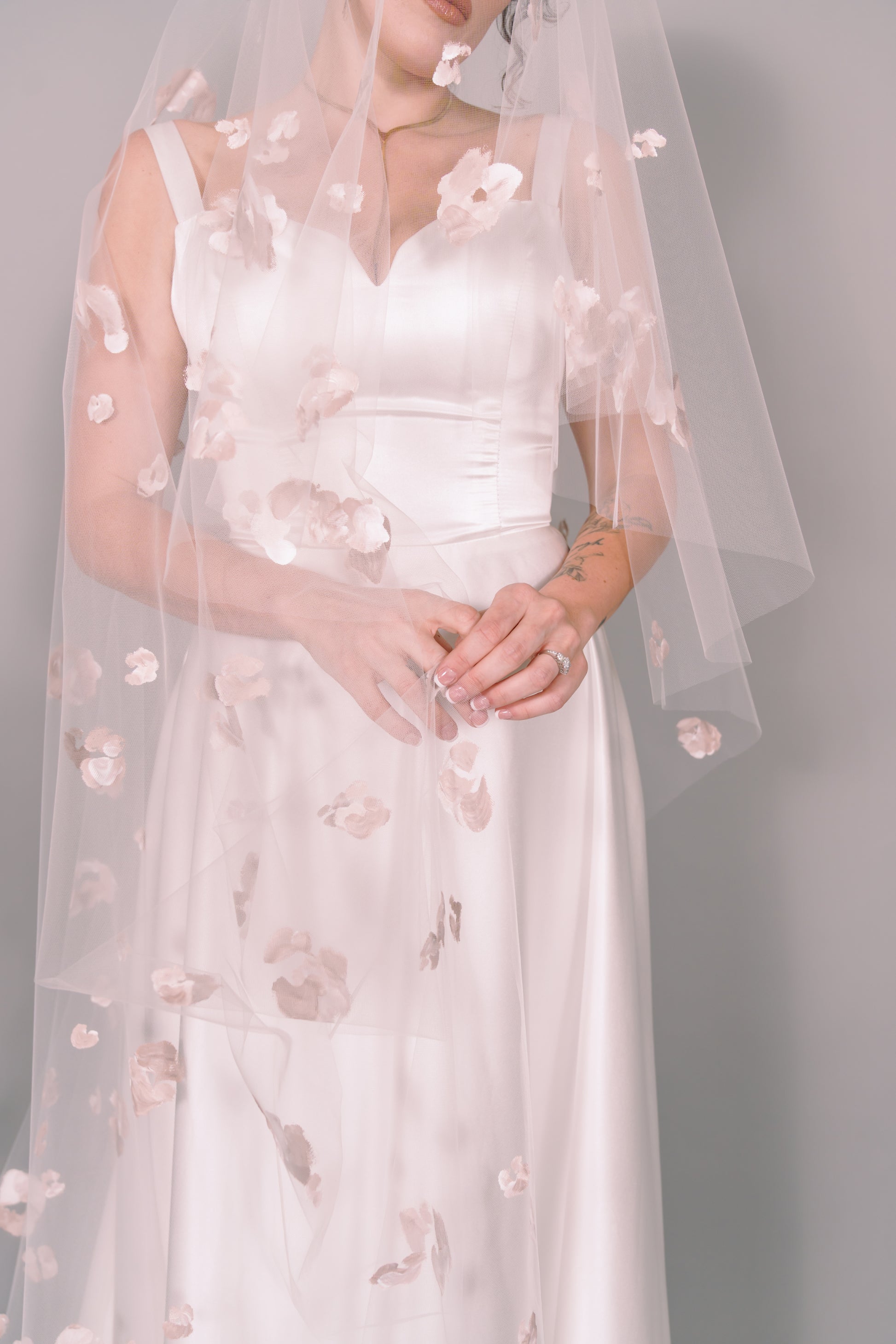 Woman wearing a wedding dress and ivory veil with painted taupe floral petals on a plain background. Photography by Rachel Sakakeeny Model is Isabelle Paulino
