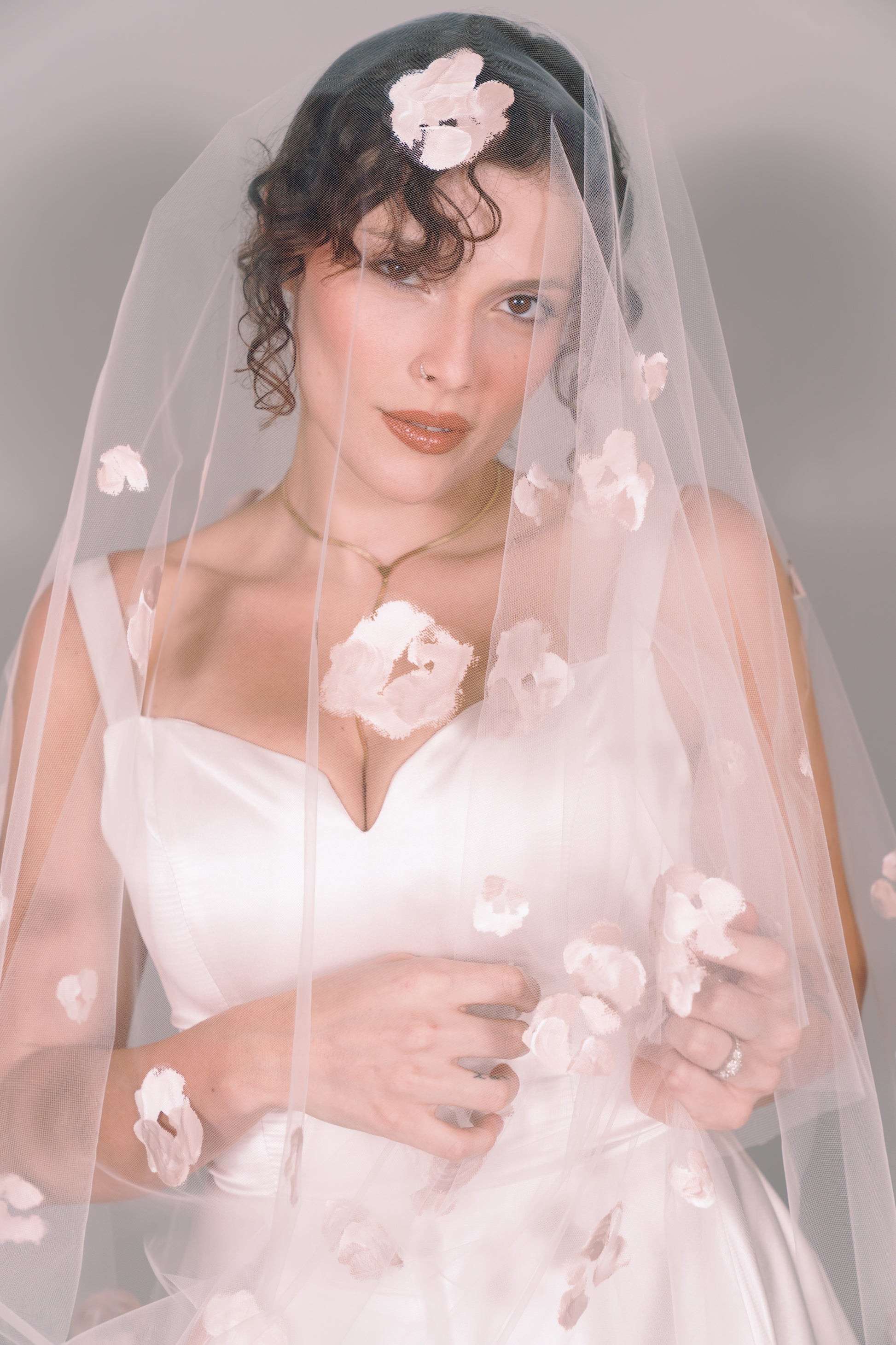 Woman wearing a wedding dress and ivory veil with painted taupe floral petals on a plain background. Photography by Rachel Sakakeeny Model is Isabelle Paulino