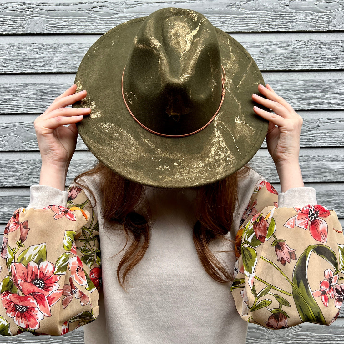 Model wearing taupe tan sweatshirt with pretty floral puff sleeves with olive green gold marbled wide flat brim rancher hat