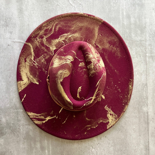 Overhead view of maroon wide brim flat brim felt rancher hat with artistic gold paint marbling.
